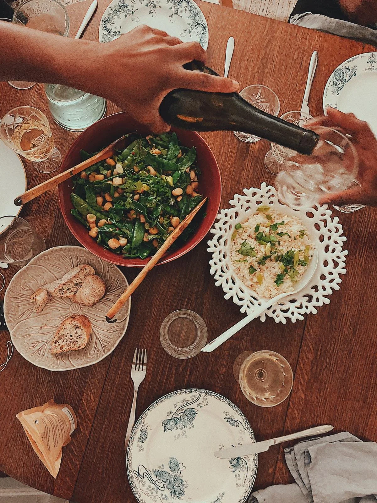 People serving and eating a meal that includes a salad, rice, and bread at a dining table with plates, glasses, and utensils.