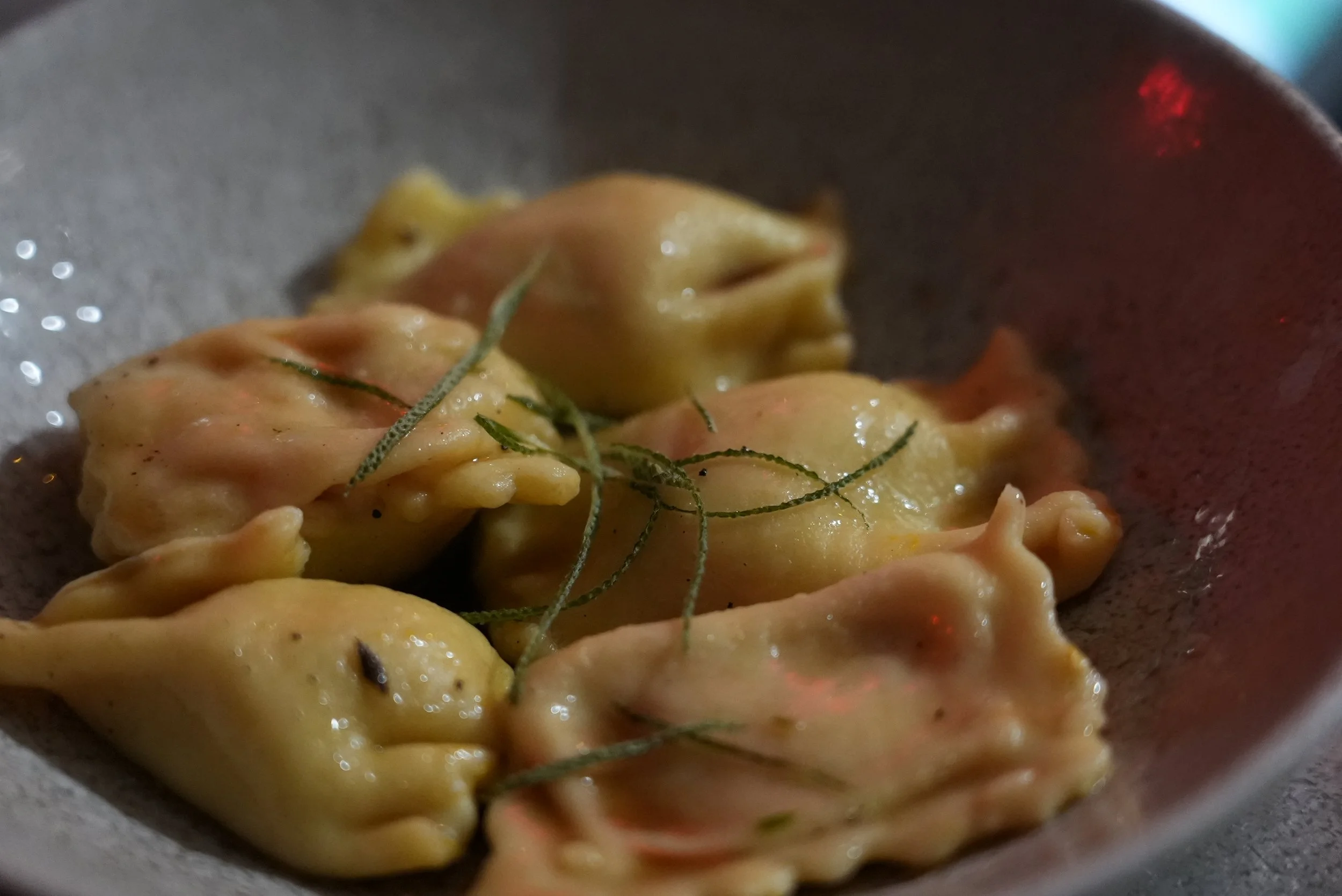 Close-up of fresh, uncooked frogs in a bowl, with some herbs on top.