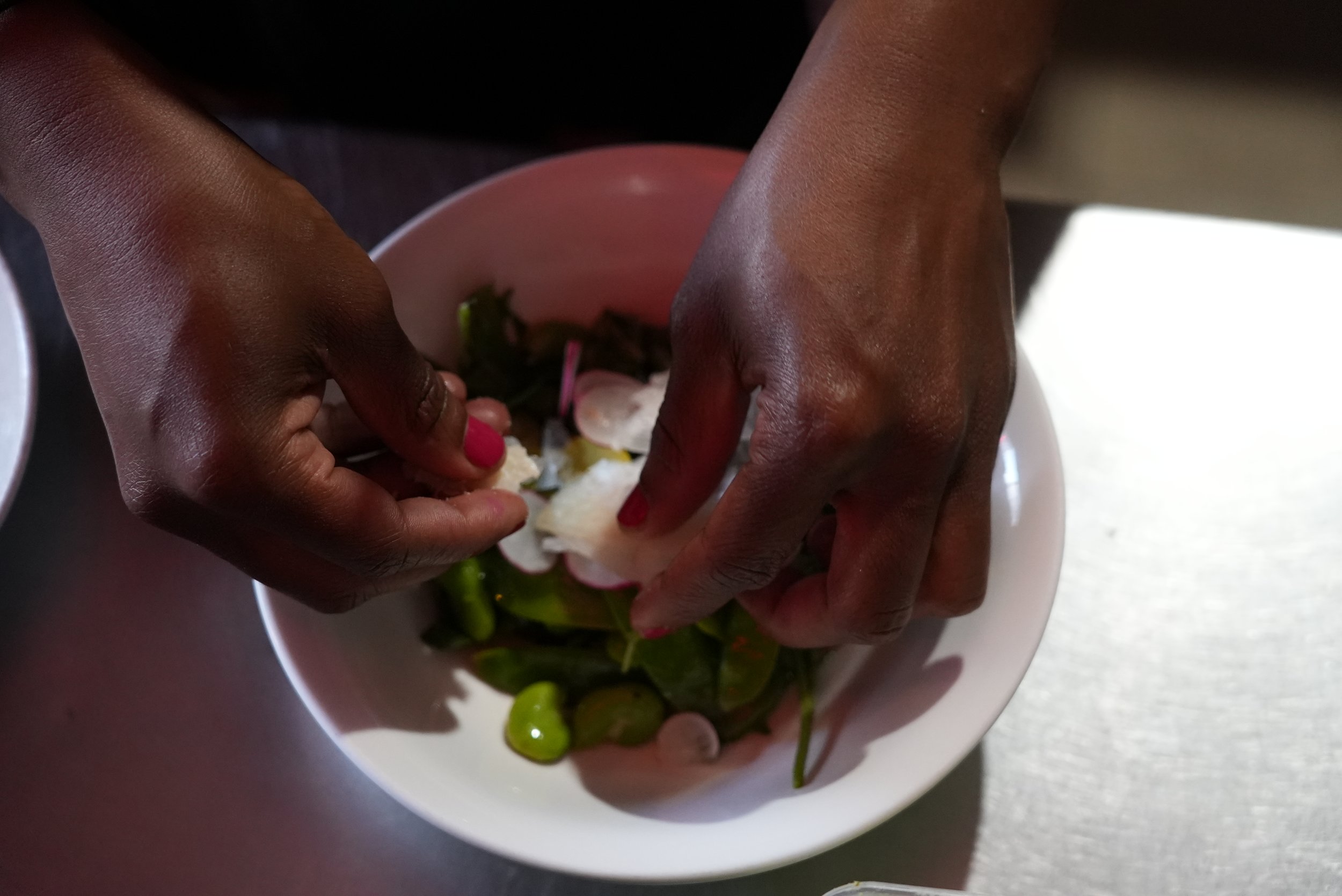 Close-up of hands squeezing a lime into a bowl with chopped vegetables, including green peppers and onions.