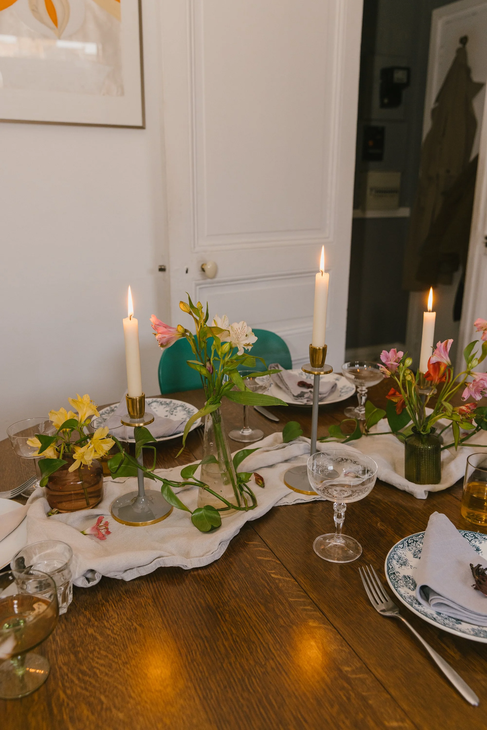 A dining table set with plates, glasses, silverware, and floral centerpieces with lit candles in gold holders.