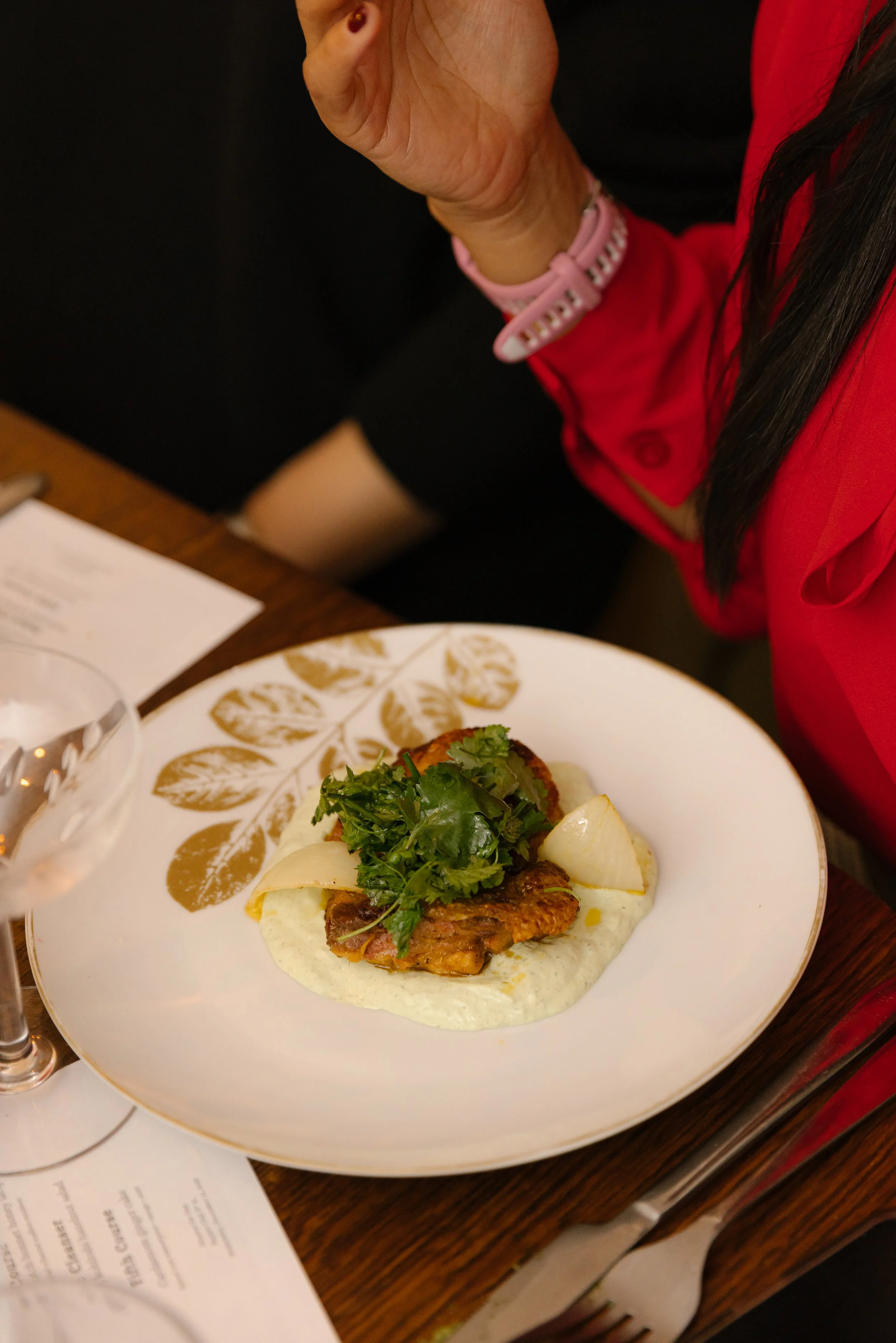 A plated dish with seasoned meat, herbs, chopped potatoes, and sauce, garnished with parsley, on a decorative white plate.