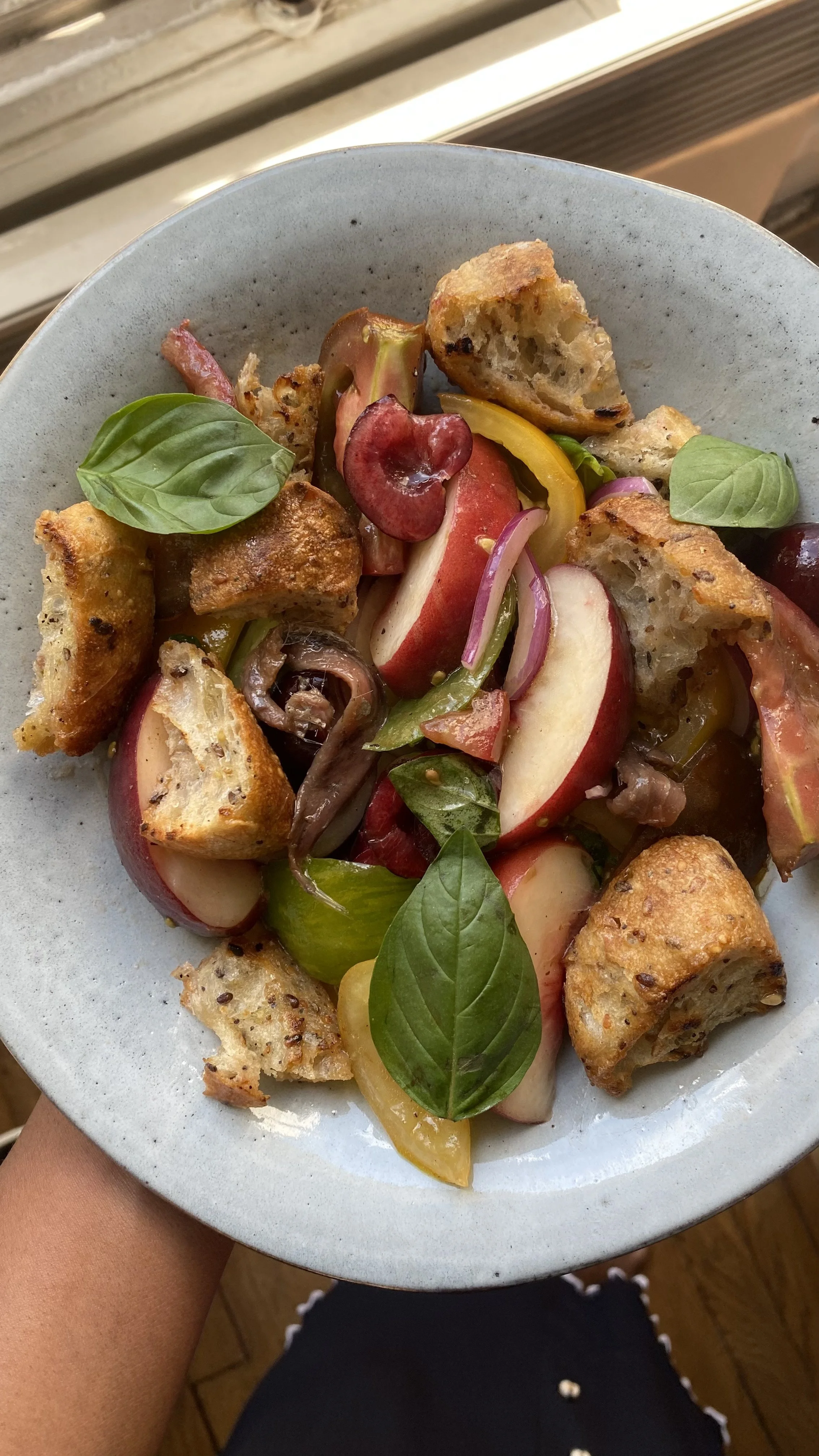 A bowl of fresh fruit and bread pieces, including sliced apples, grapes, and basil leaves.