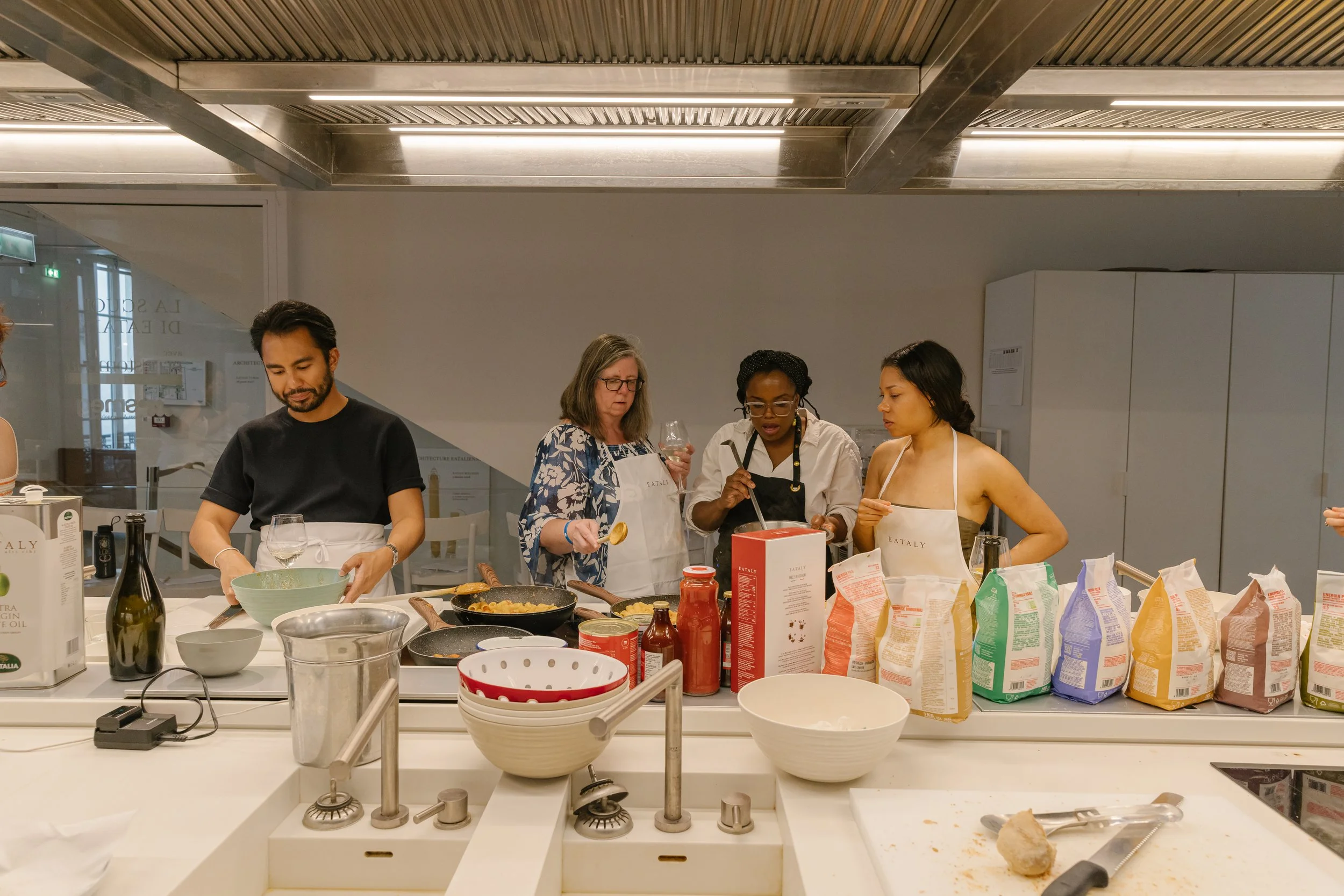 A group of four diverse people cooking together in a modern kitchen, surrounded by various ingredients and kitchen utensils.
