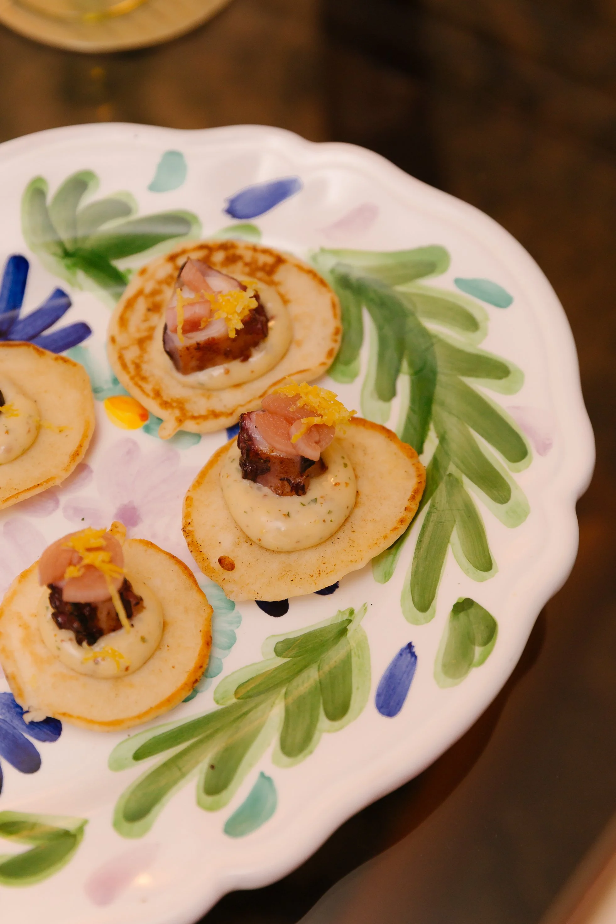 Close-up of a decorative plate with small appetizers topped with meat, lemon, and herbs.