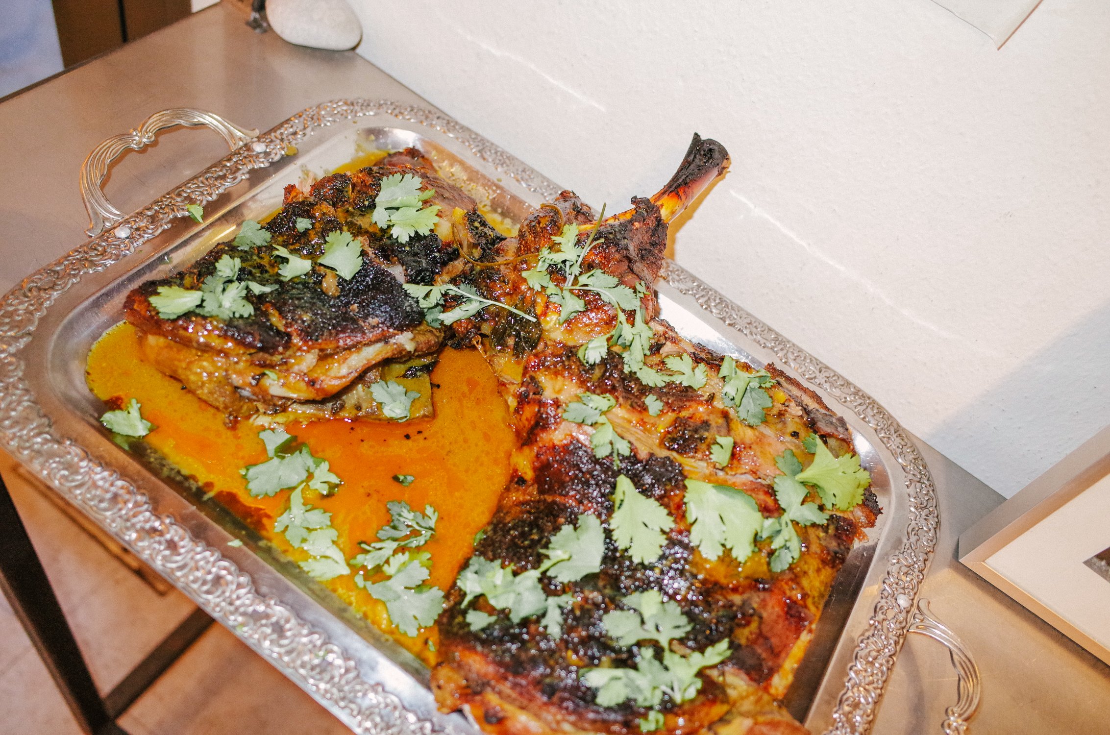A roasted fish garnished with cilantro on a silver ornate serving tray with a yellow sauce underneath.