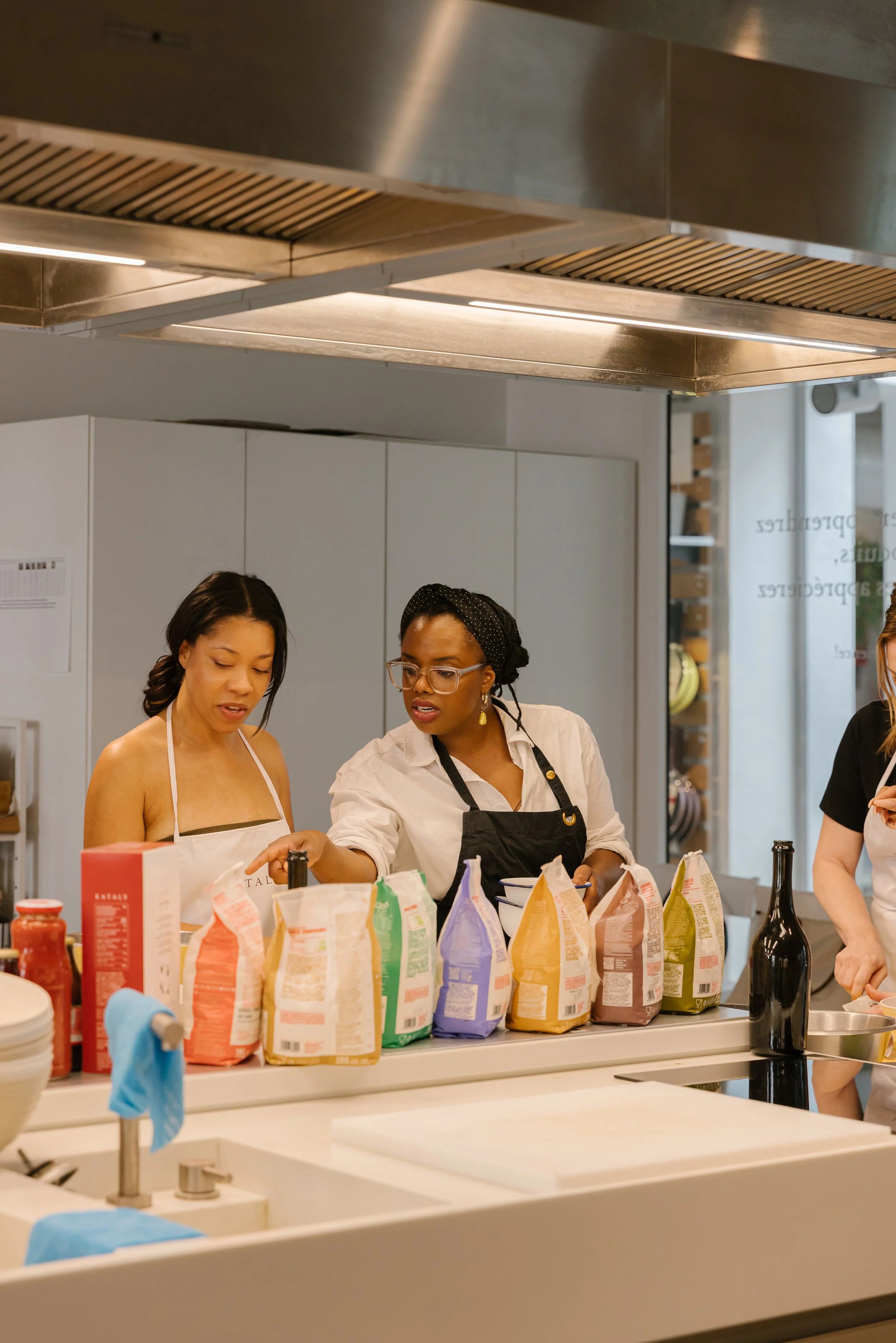Women cooking and preparing food in a modern kitchen with various ingredients and kitchen utensils on the counter.