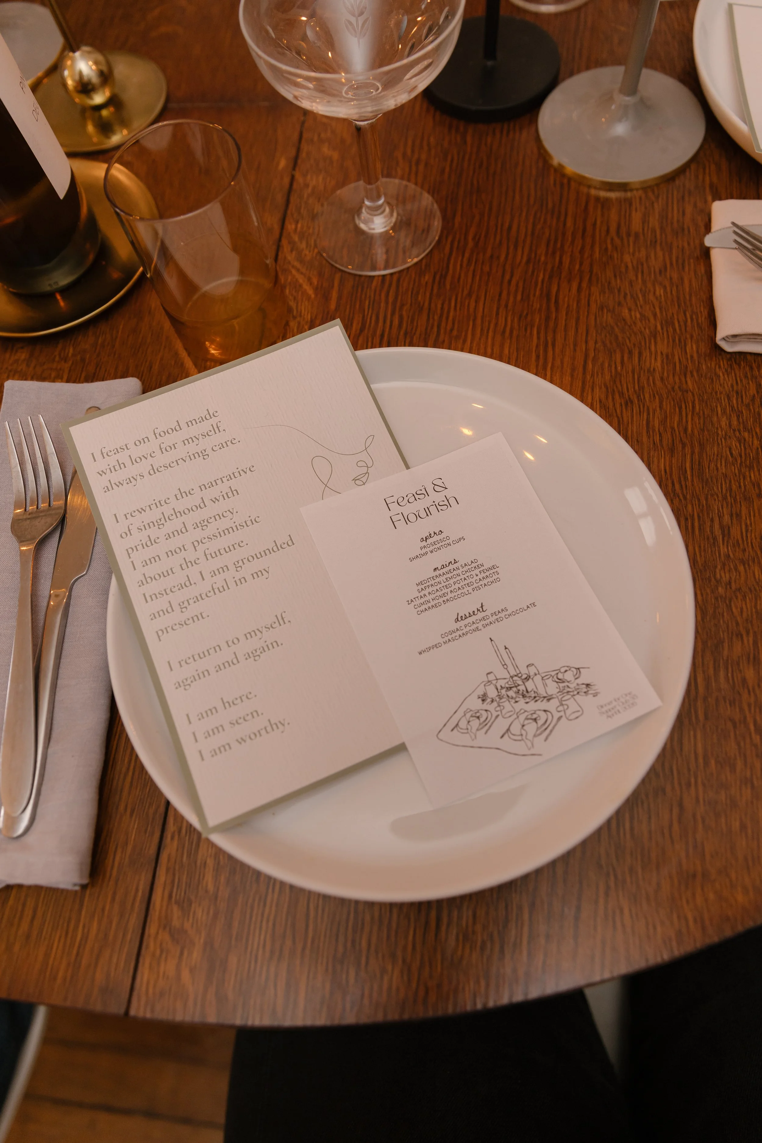 A dinner table setting with a menu, a glass of water, a champagne flute, a fork, a knife, and a napkin. The menu features text and an illustration of a plate of food, with the title 'Feast & Flourish.'