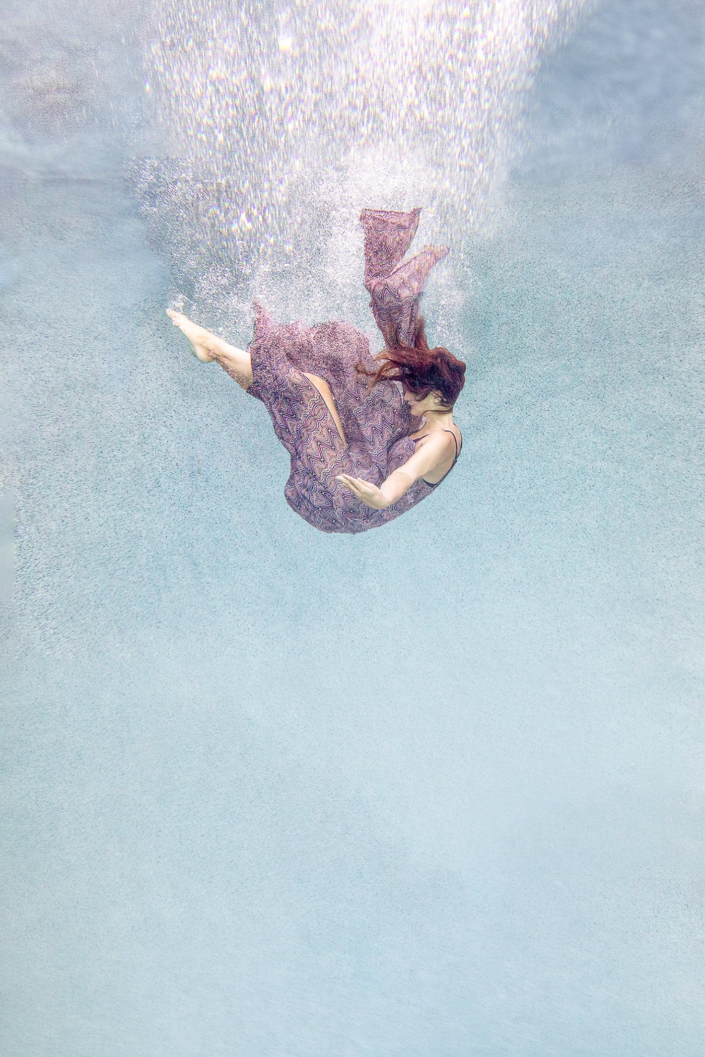 Woman falling backward underwater in an ethereal fine art photograph, expressing release, trust, and freedom