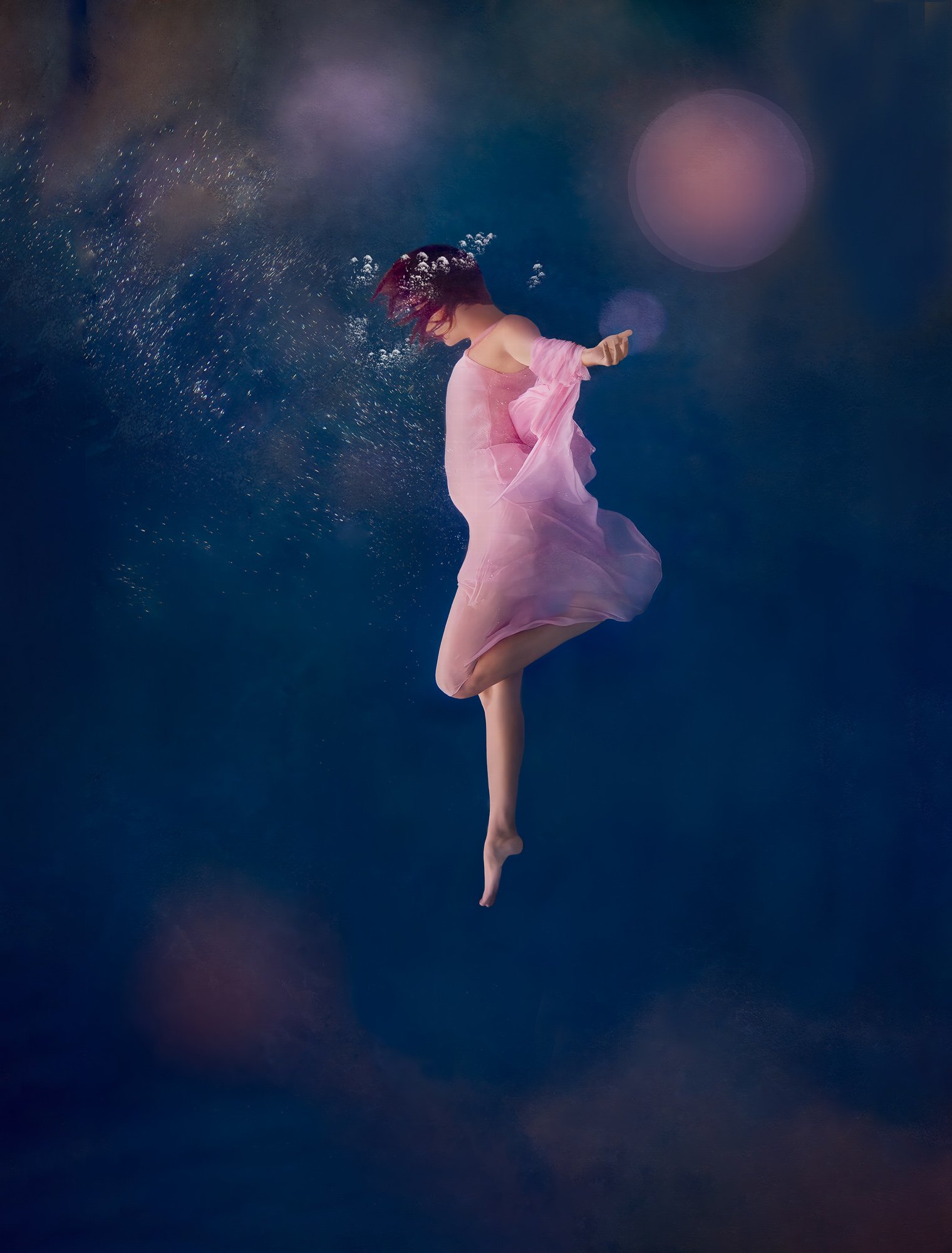 Fine art underwater portrait of a woman dancing in a pink dress underwater with bubbles and soft reflections of pink and orange