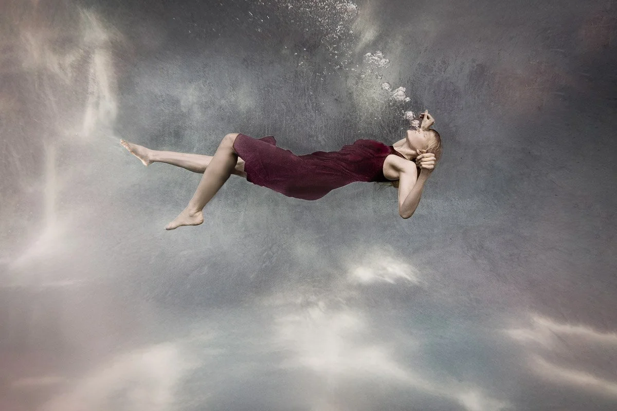 Woman swimming underwater on her back in a purple dress with light refractions and bubbles, fine art underwater photography