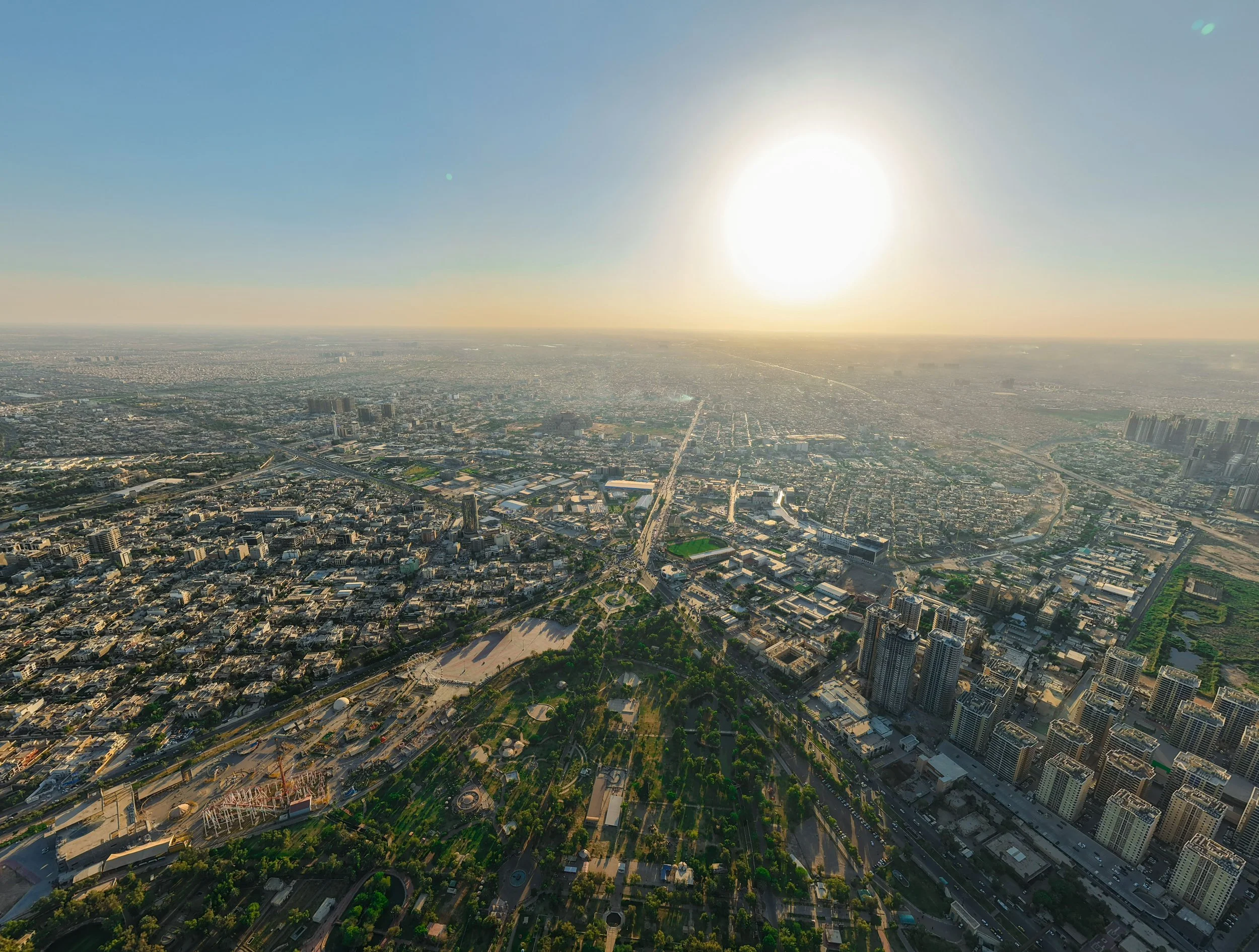 An aerial view of a densely built city at sunset, showing extensive urban development surrounding a large central park, illustrating the contrast between impervious surfaces and urban green space.