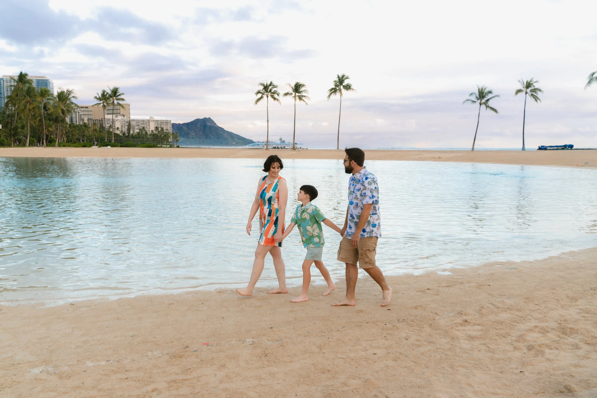 Multi-generational family posing beside Hilton Lagoon at sunrise with palm trees and the Waikiki shoreline in the background.