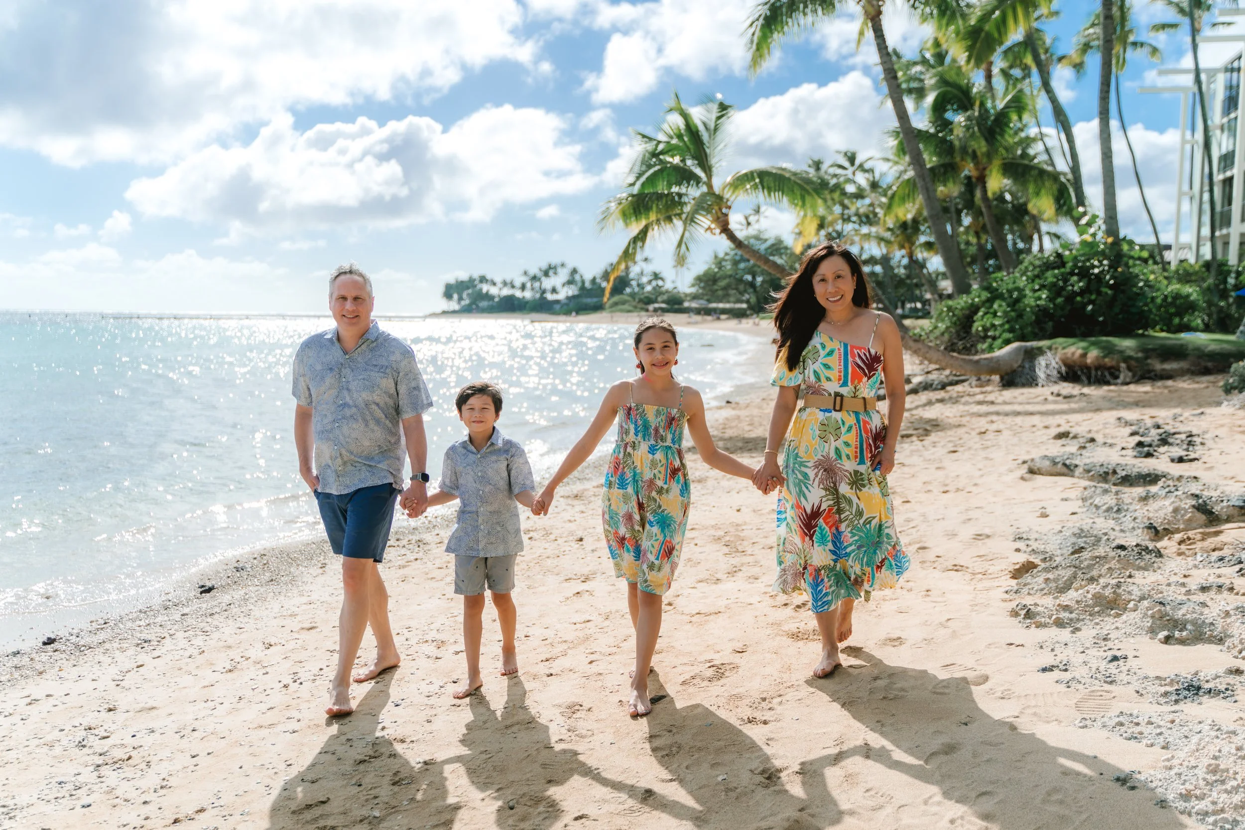 Family posing together on the beach with palm trees and ocean views during an Oahu beach family photography session in Kahala.