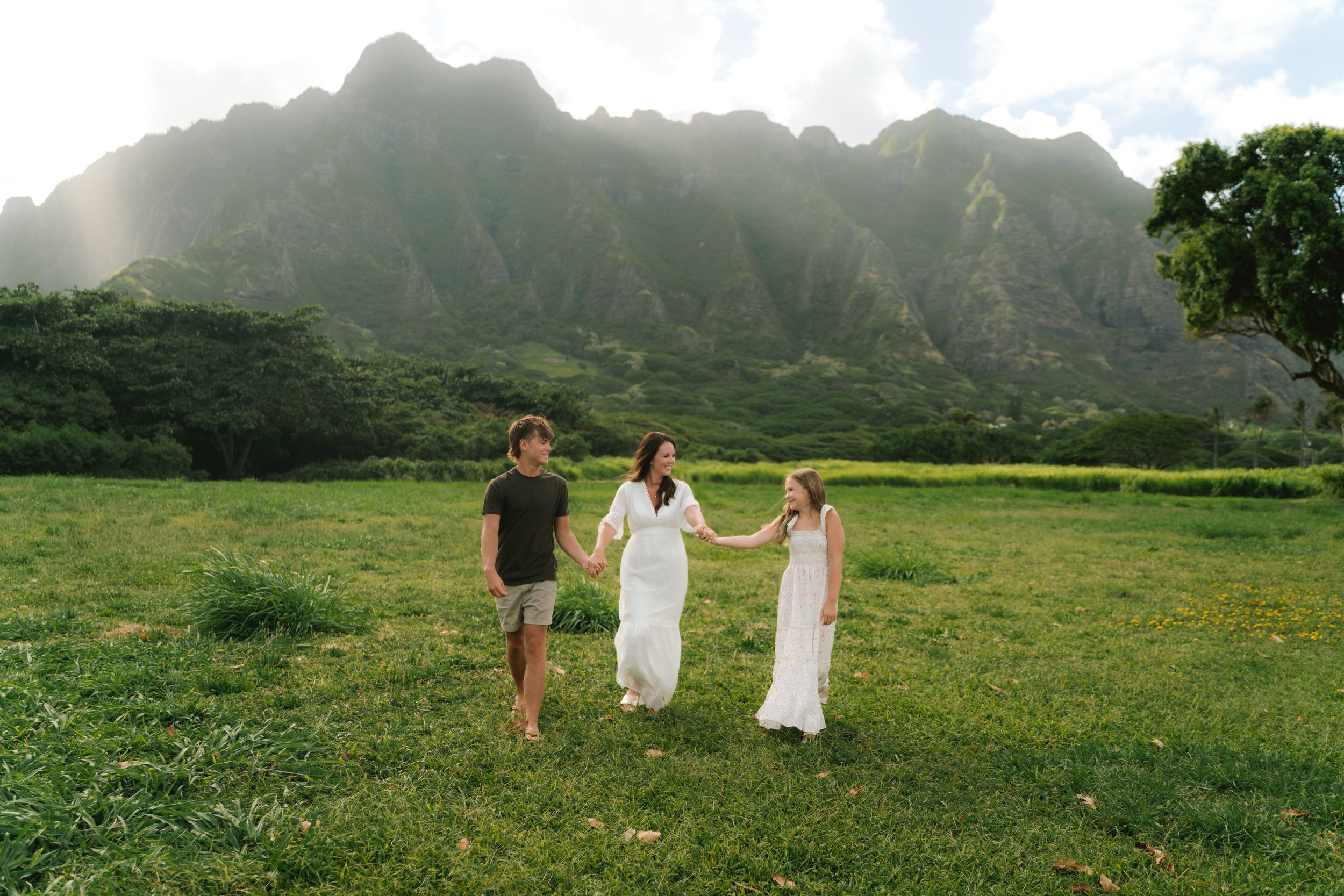 Candid family photo captured at Kualoa Regional Park with lush green mountains and tropical scenery