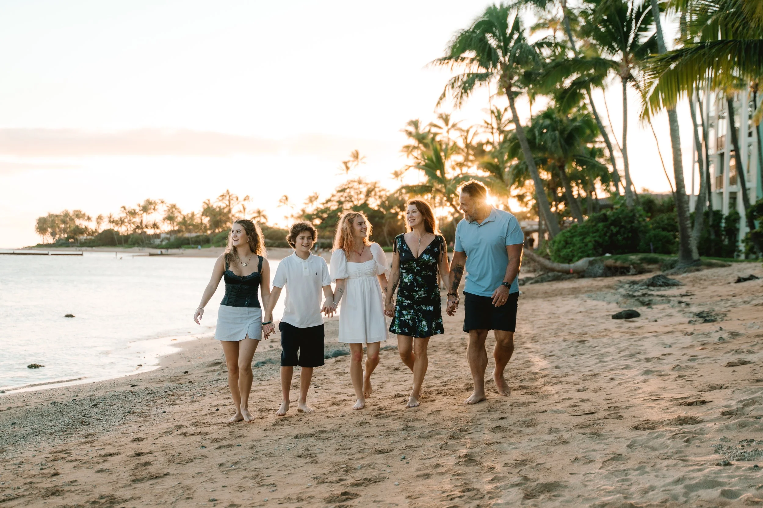 Family enjoying a sunset beach session with palm trees and ocean views during an Oahu family photographer shoot at Kahala Beach.