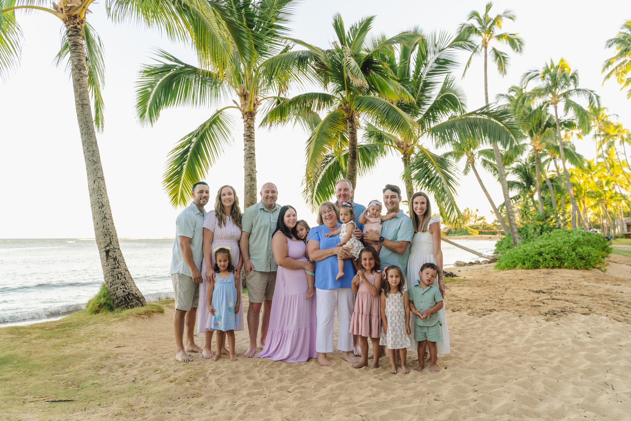 Family enjoying a sunset photoshoot at Kahala Beach on Oahu with golden skies, palm trees, and ocean views.