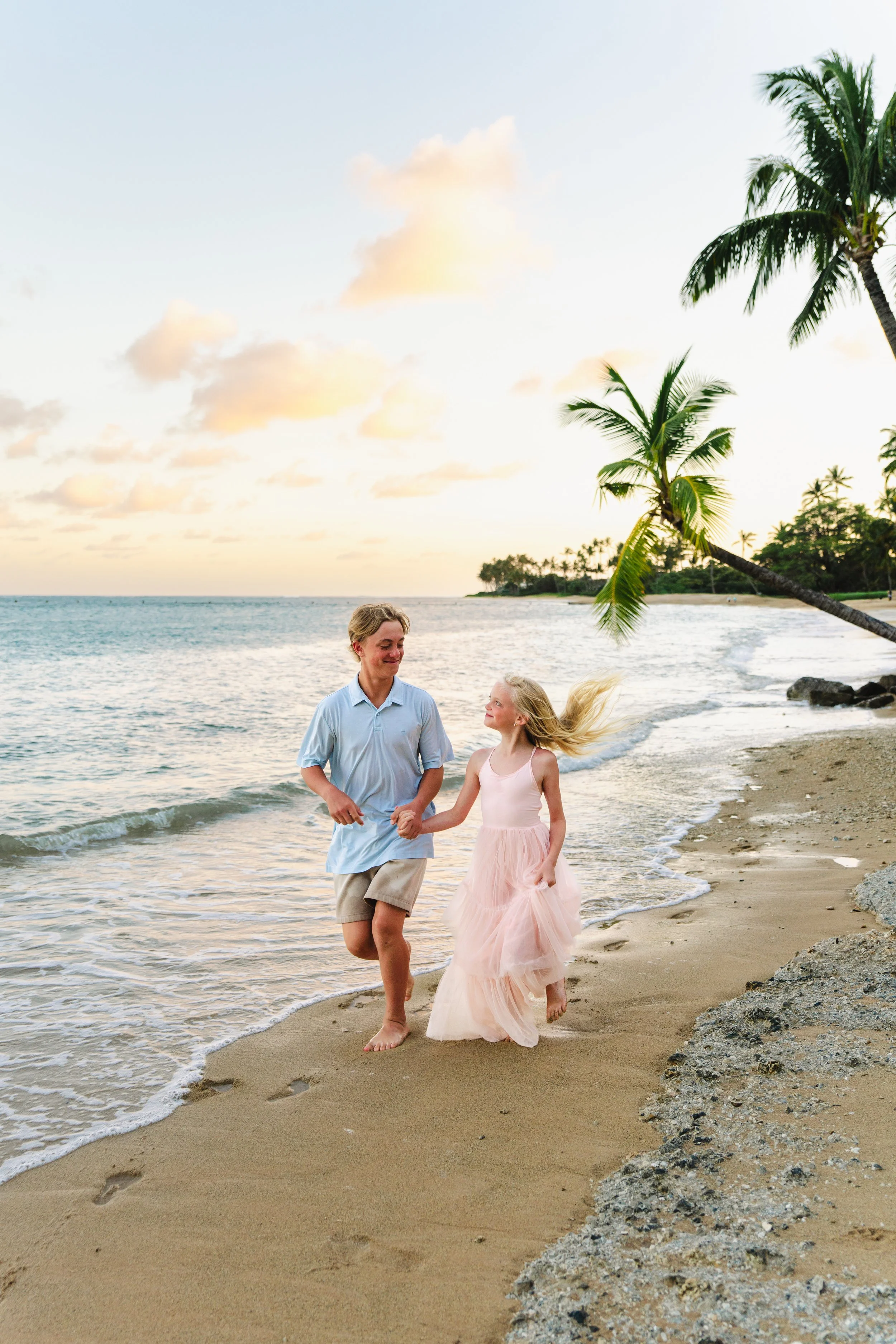 Two siblings running and being photographed together at sunset on beautiful Kahala Beach in Oahu