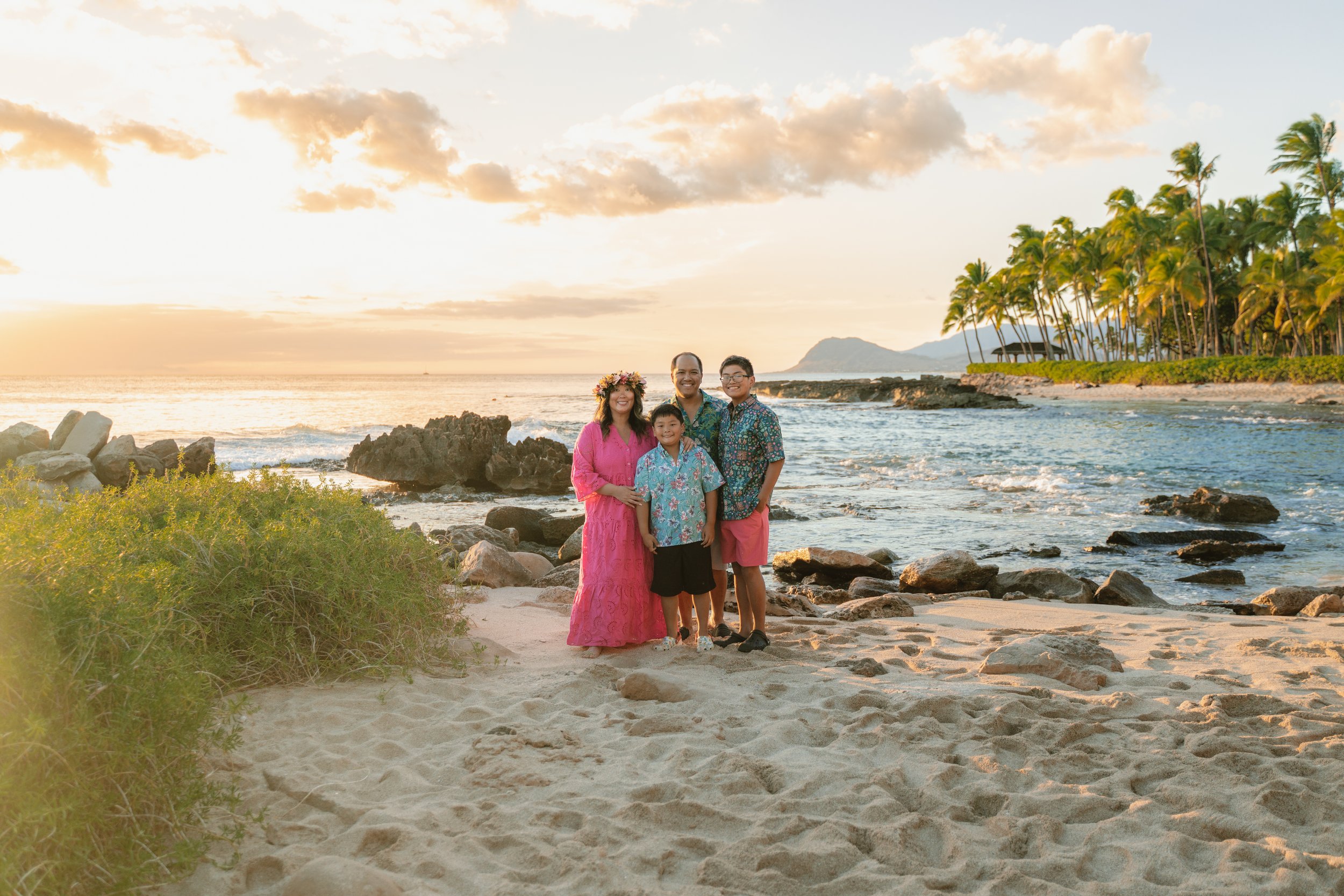 Family together at sunset with ocean and palm trees during family photos on Oahu at Secret Beach in Ko Olina near Disney Aulani.