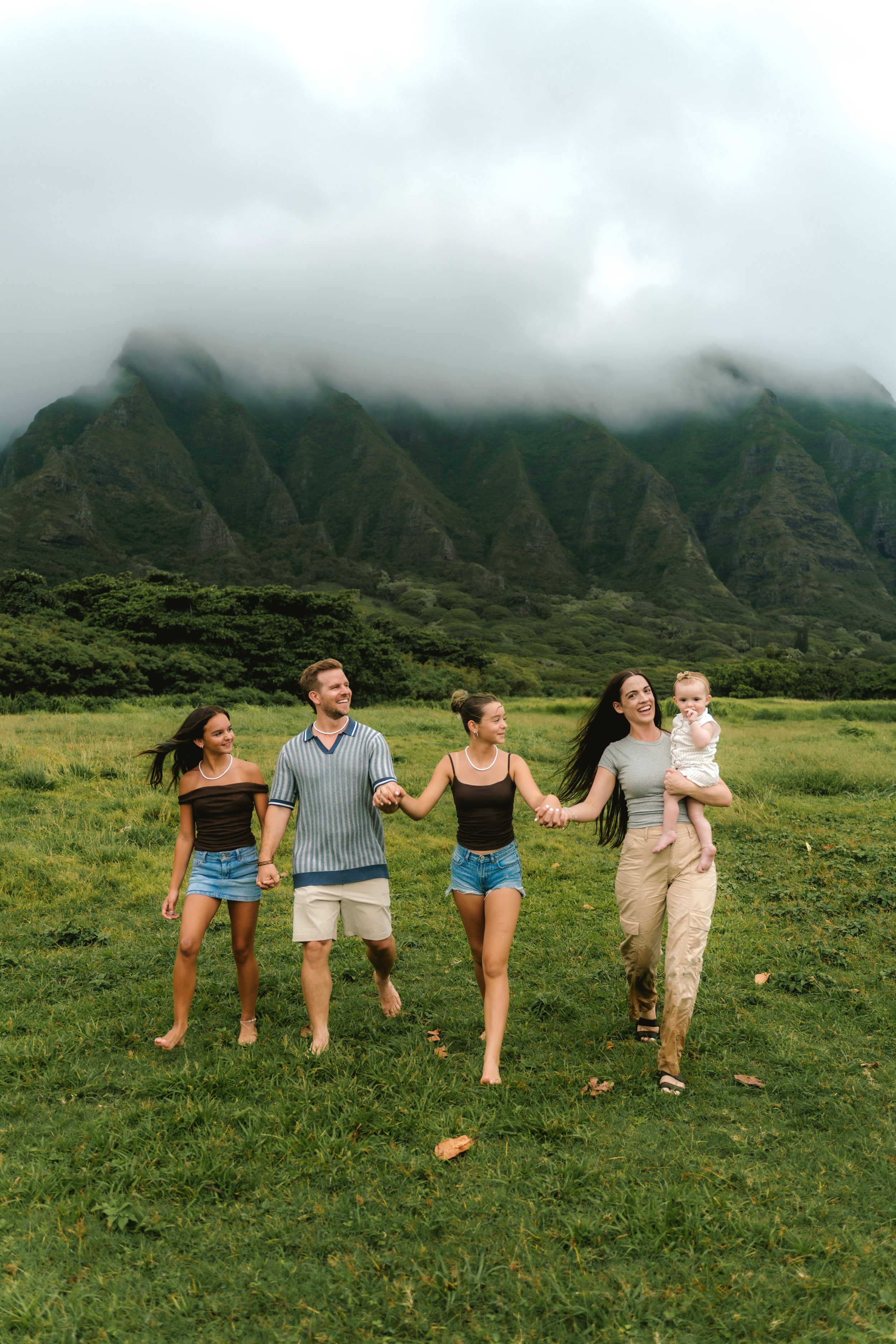 Family of five smiling together at Kualoa Regional Park with the Koʻolau Mountains in the background on Oahu.
