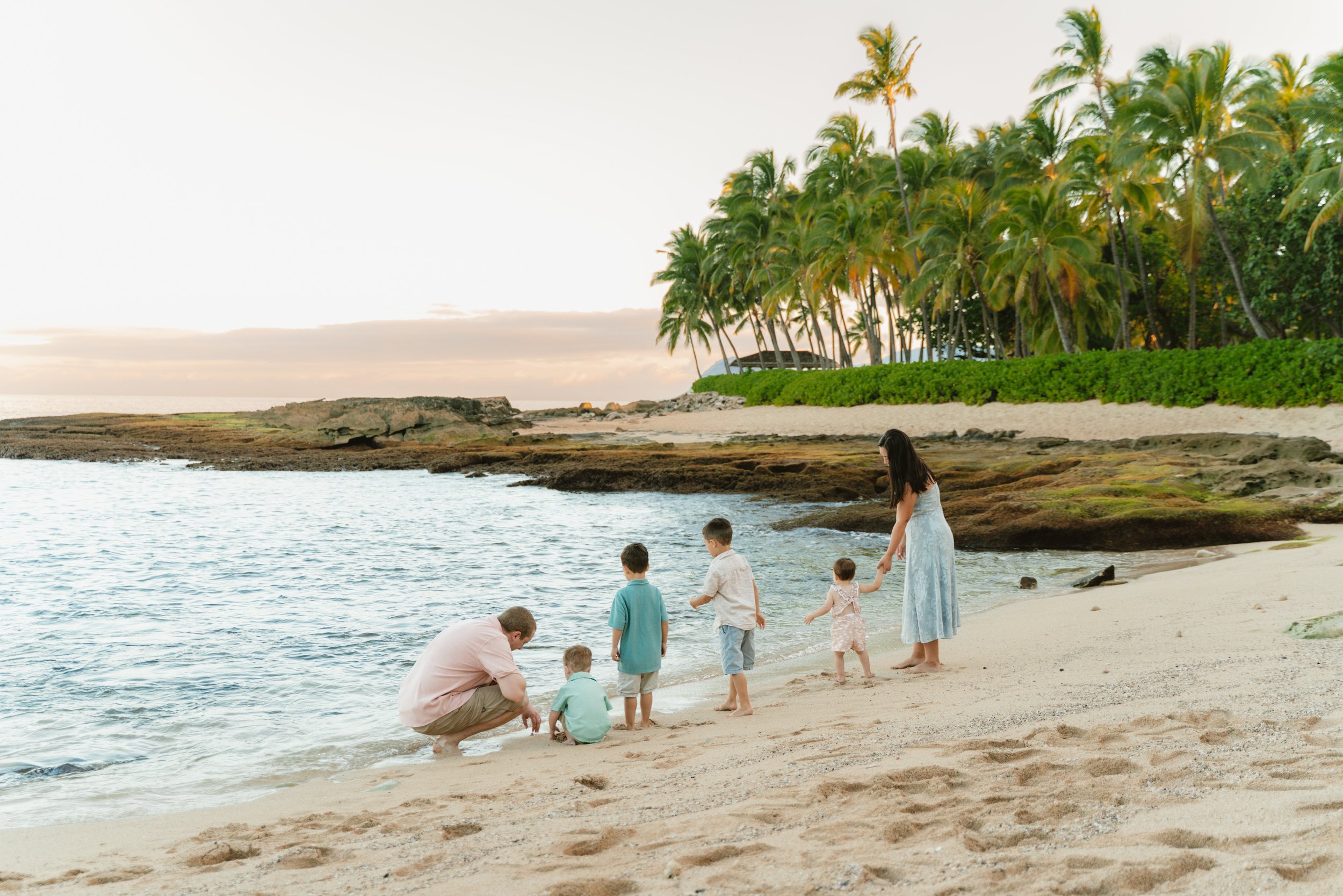 Family walking along the shoreline at Secret Beach on Oahu during sunrise with turquoise water and warm morning colors.