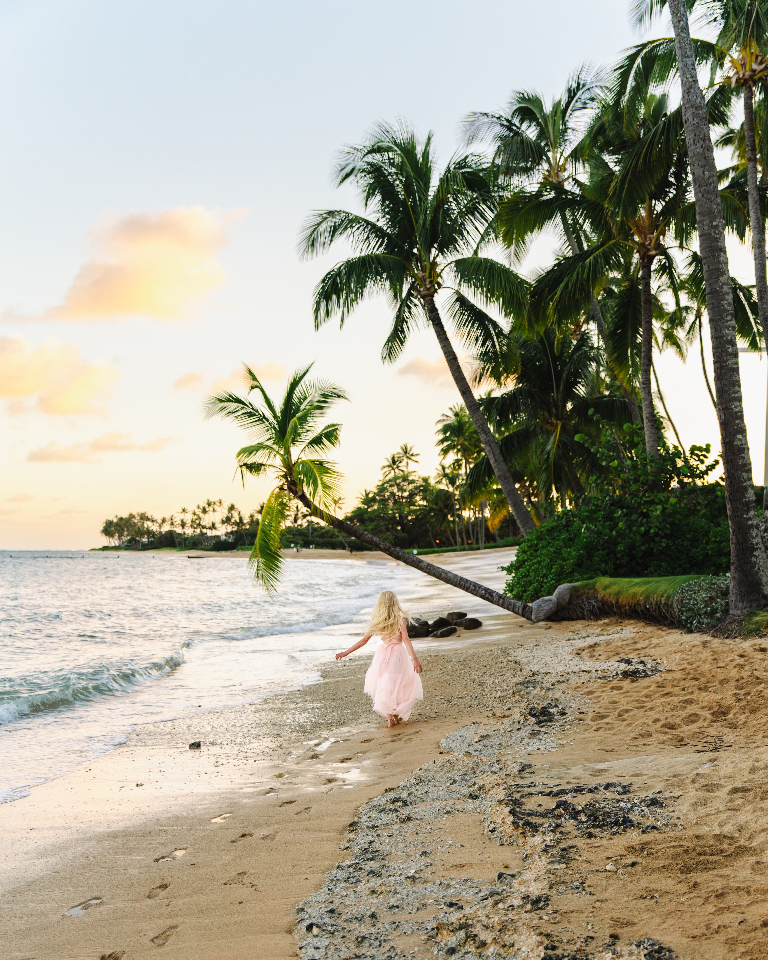 Little girl running and being photographed at sunset on beautiful Kahala Beach in Oahu
