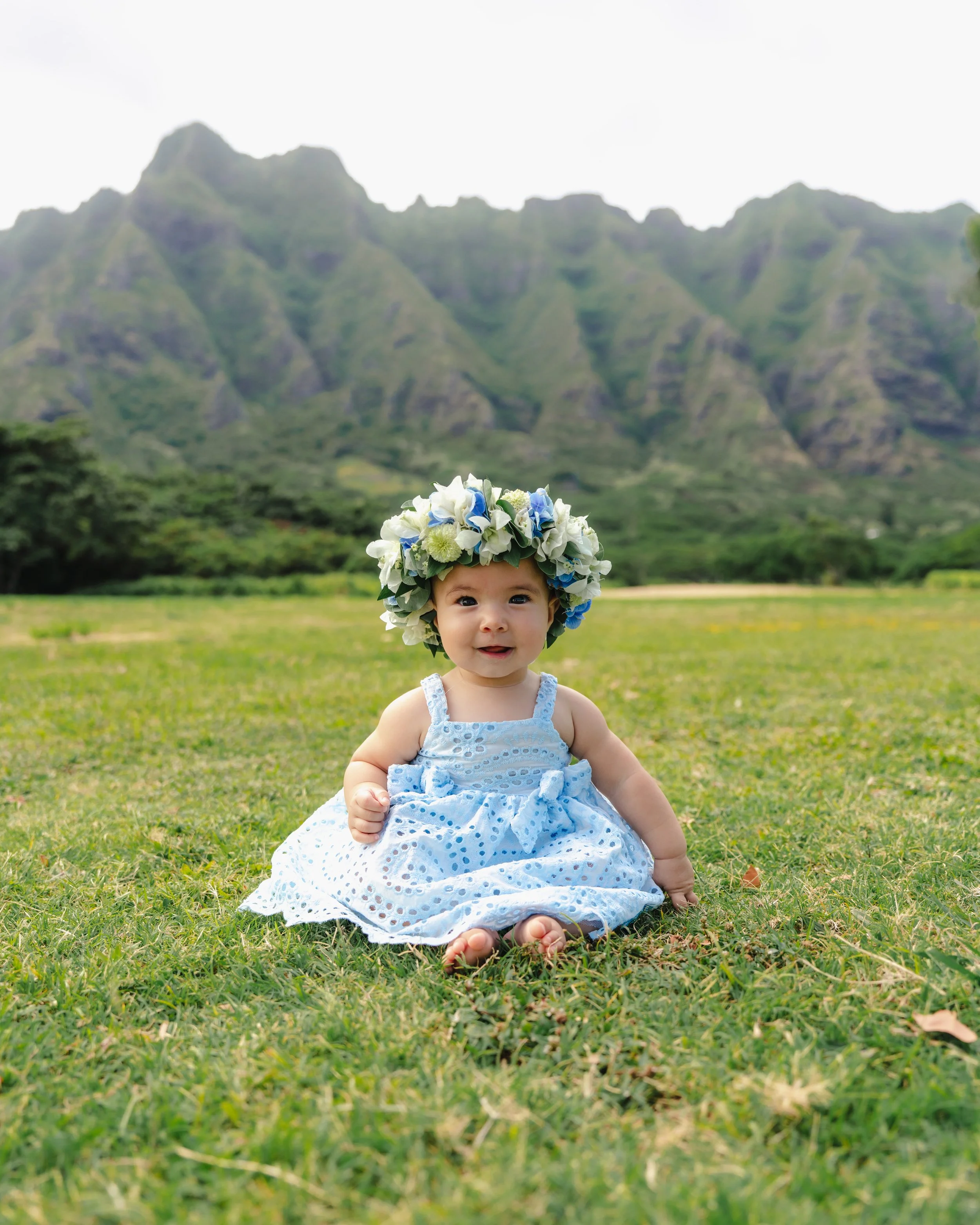 Newborn wearing a lei po'o photographed among the tropical landscape and mountains of Kualoa, Oahu