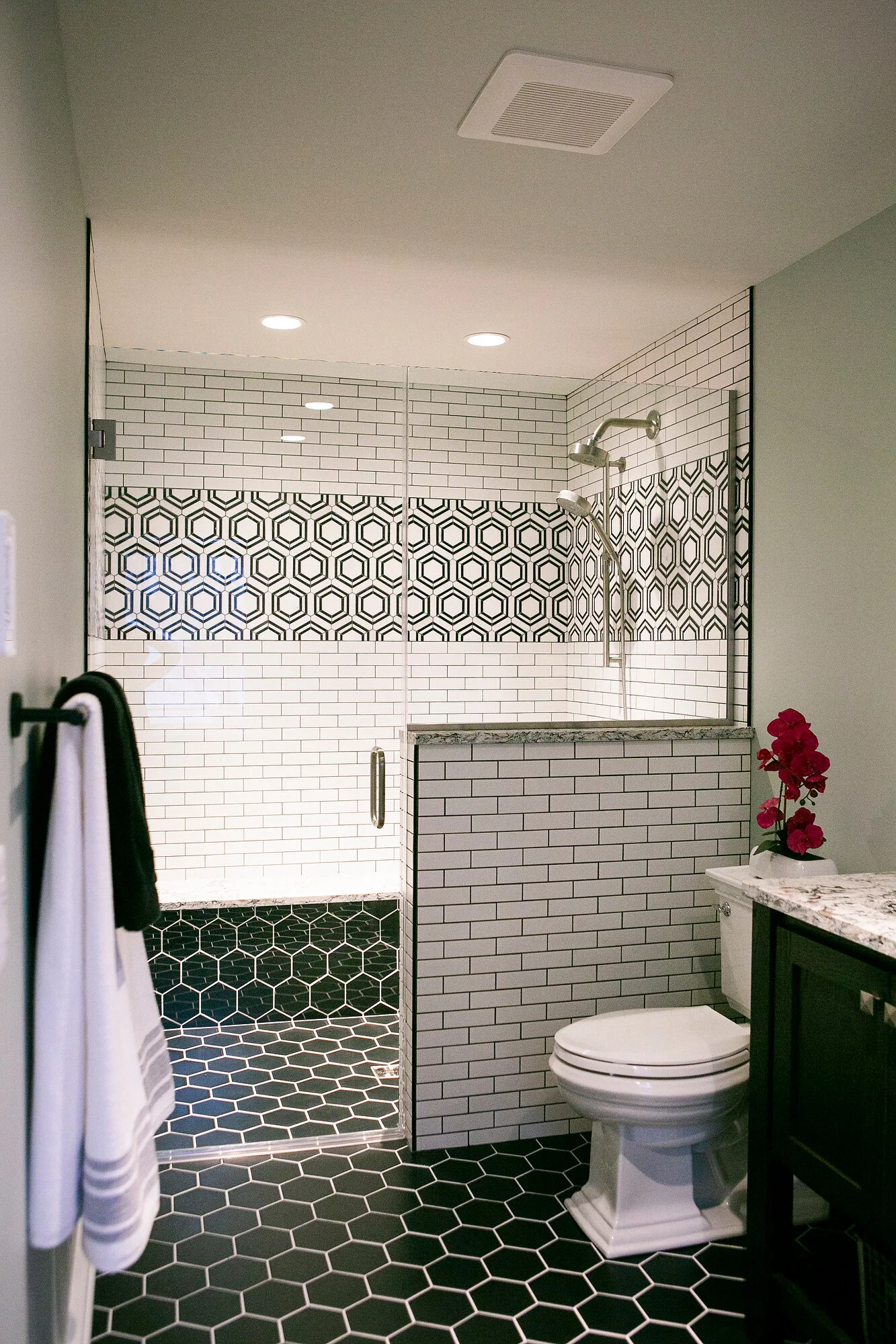 Black and white tiled shower stall with glass door and hexagon accent tiles. 