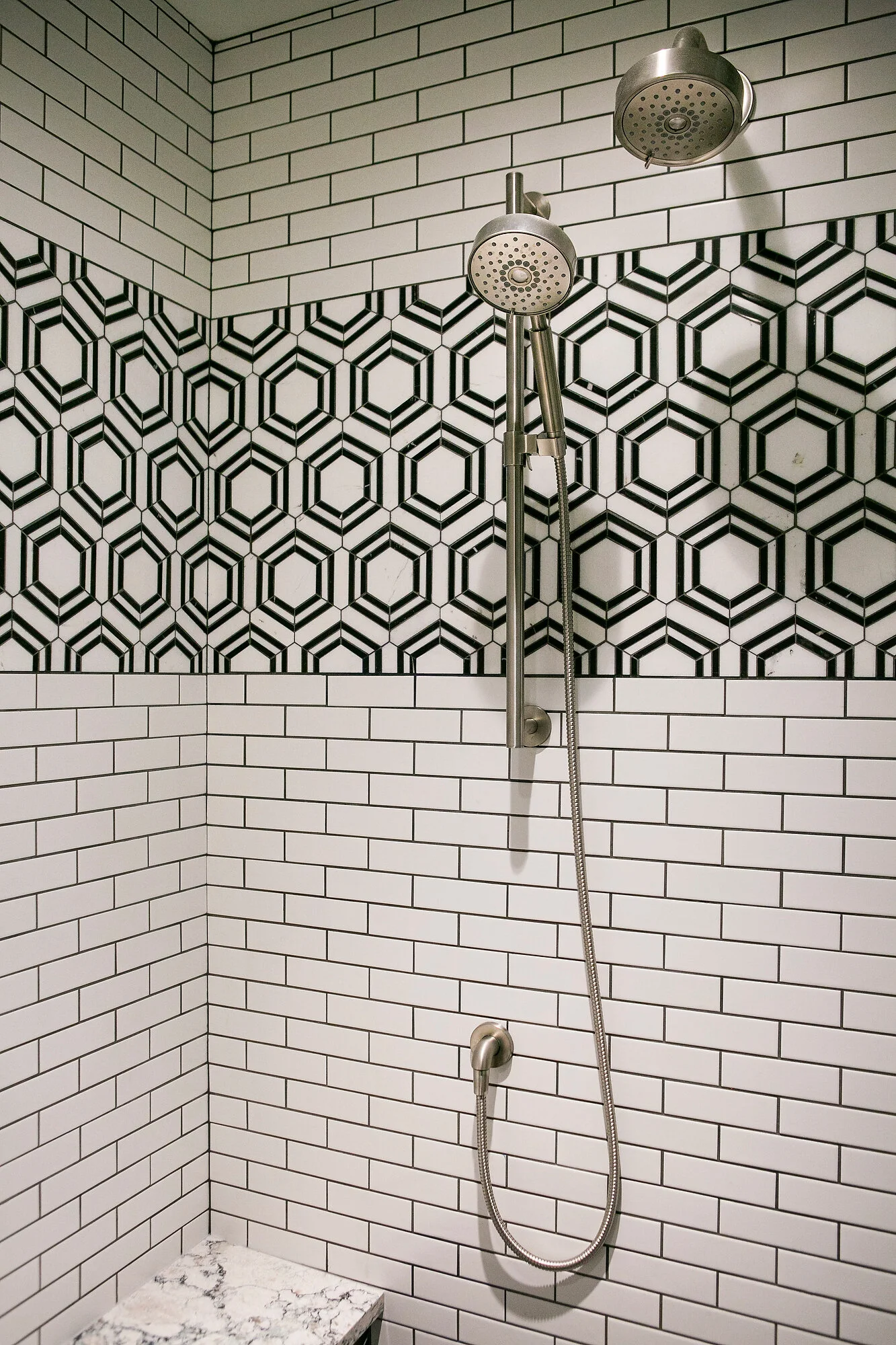  Close-up of shower stall with white subway tiles and black and white hexagon accent tiles. 