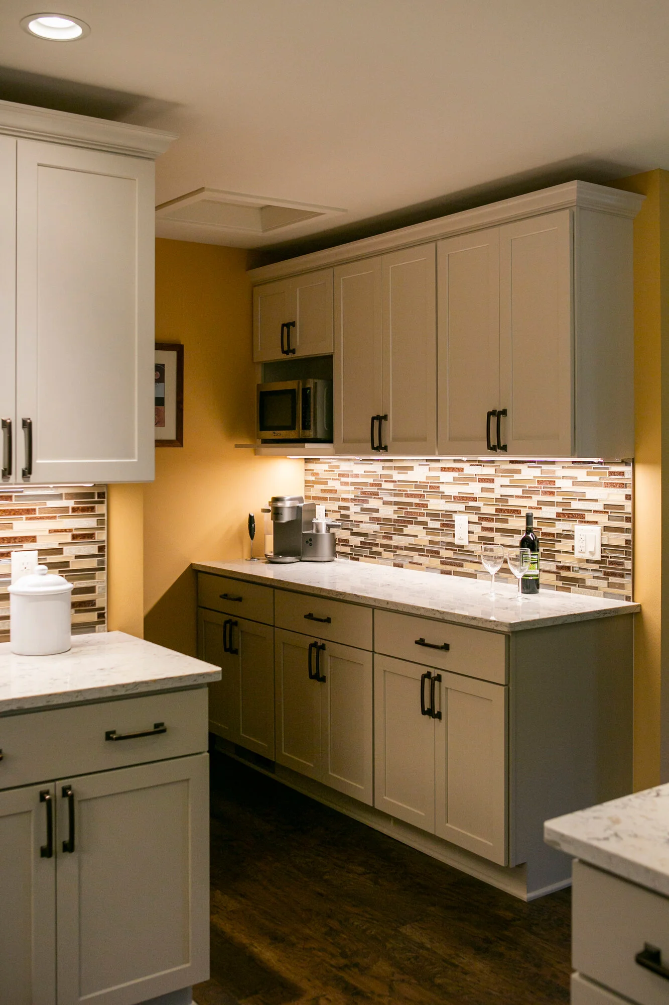  Kitchen with yellow walls, brown and cream tiled backsplash, white cabinets and white marble countertops. 