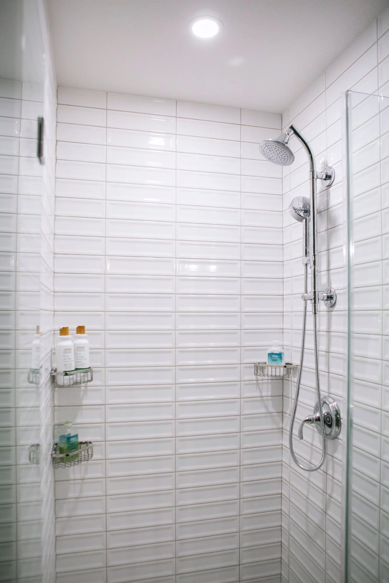  Glossy white ridged subway-tiled shower with chrome fixtures. 