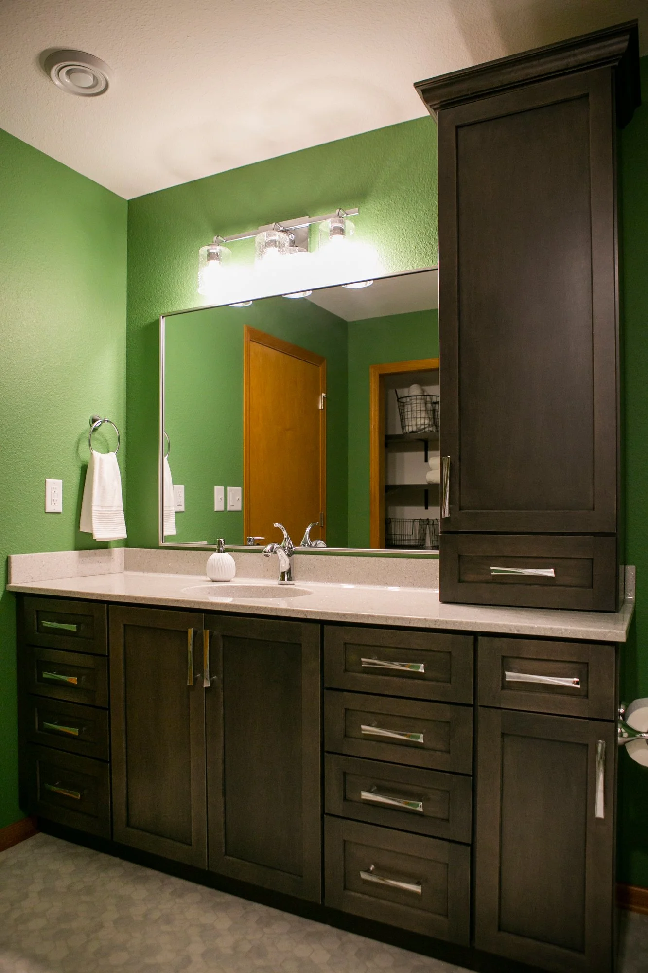  Dark wood vanity with green wall and large mirror. 