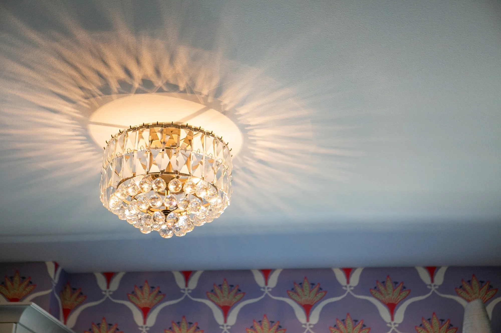  Close-up of ornate glass ceiling light in home office with bold purple patterned wallpaper. 