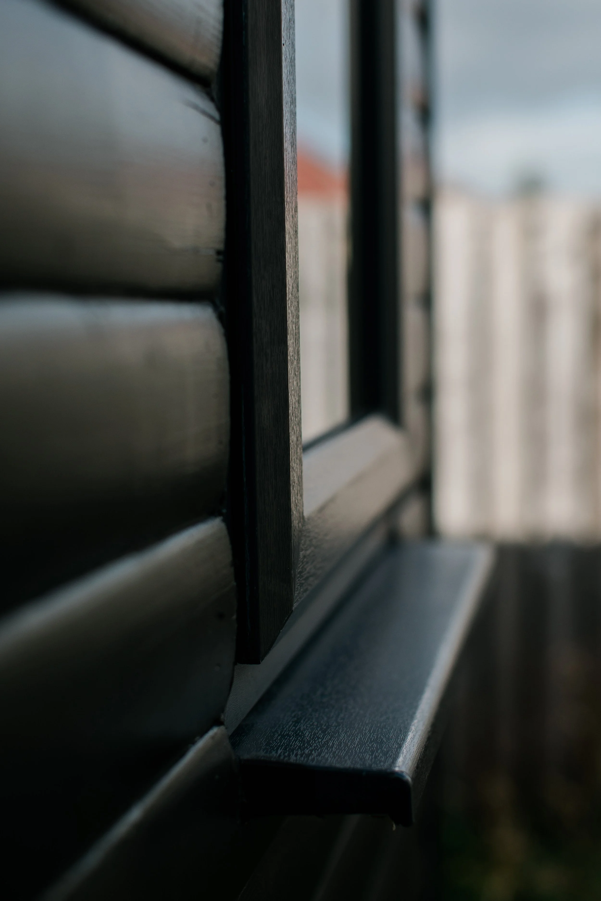 Close-up of a house window with black trim and horizontal wooden siding in the background.