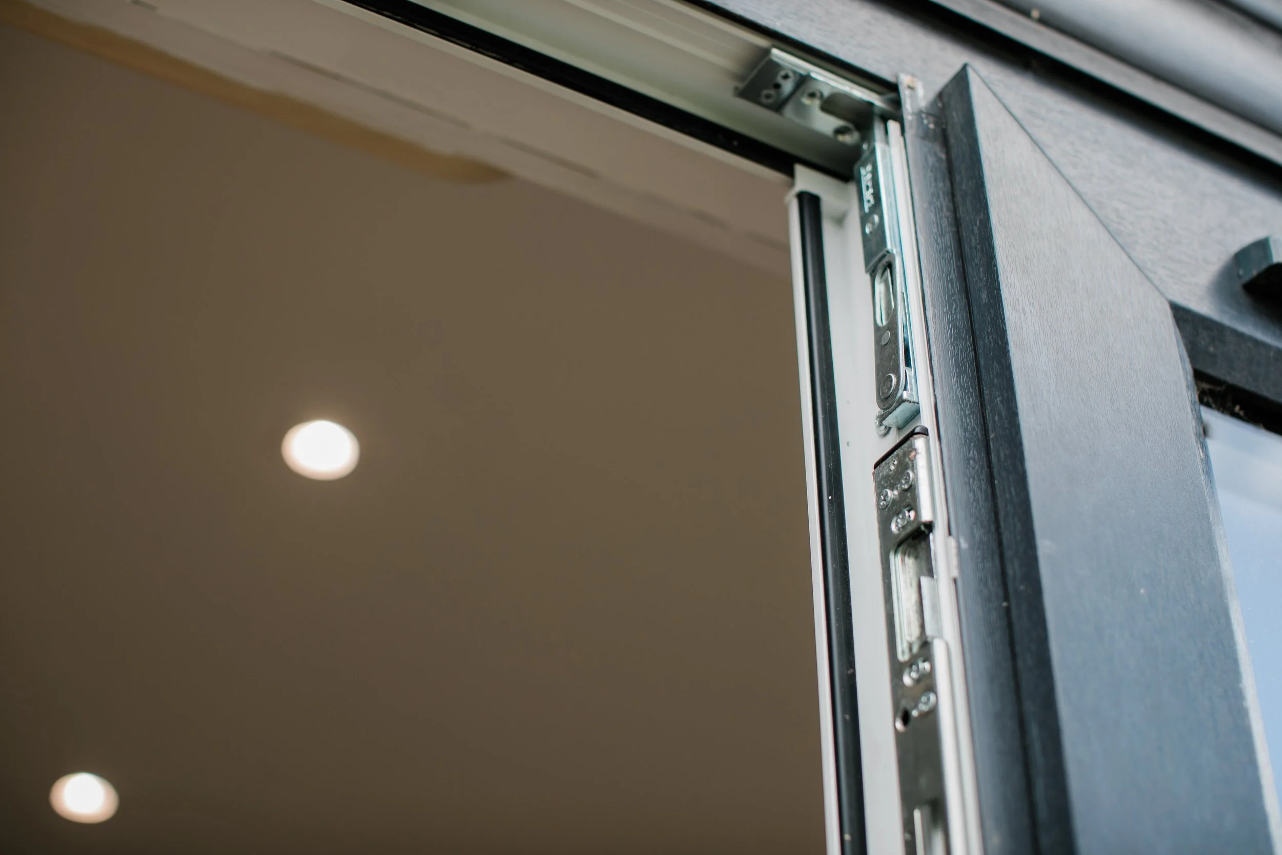 Close-up of a door frame with a metal door latch and sliding mechanism, partially open, under ceiling with recessed lighting.