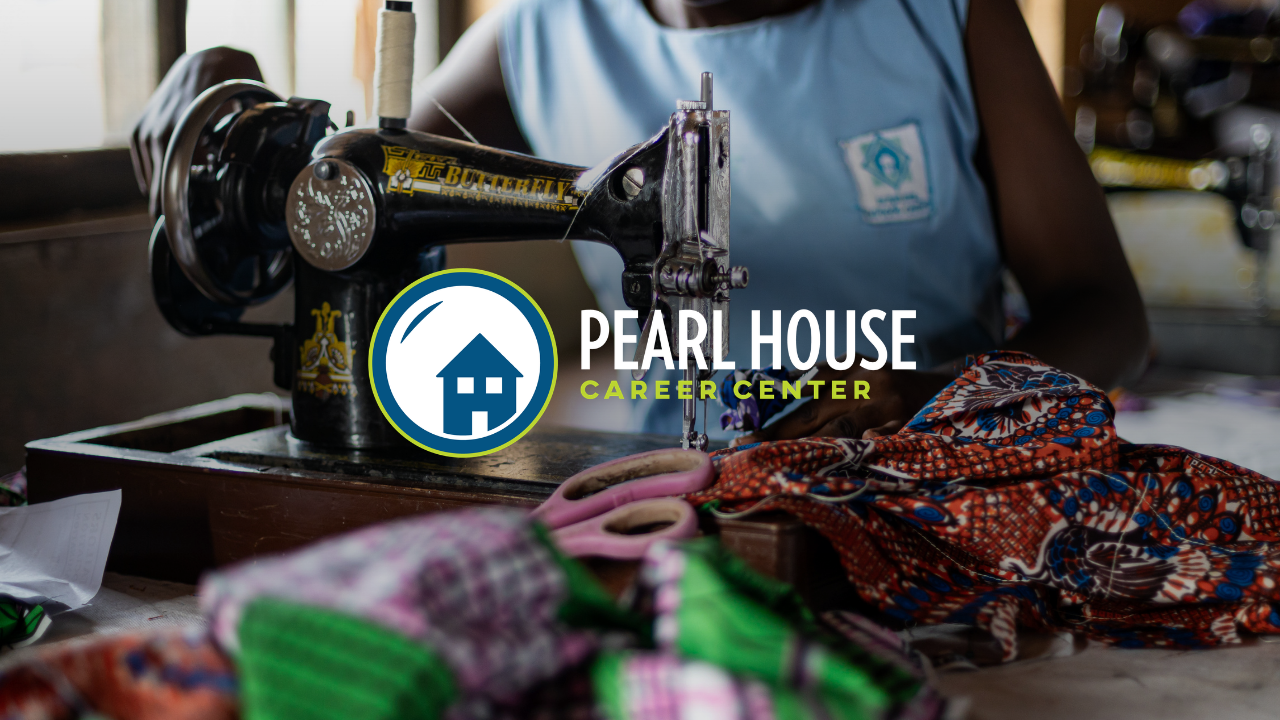 A person sewing fabric with a black industrial sewing machine, surrounded by colorful textiles and scissors, in a workshop setting.