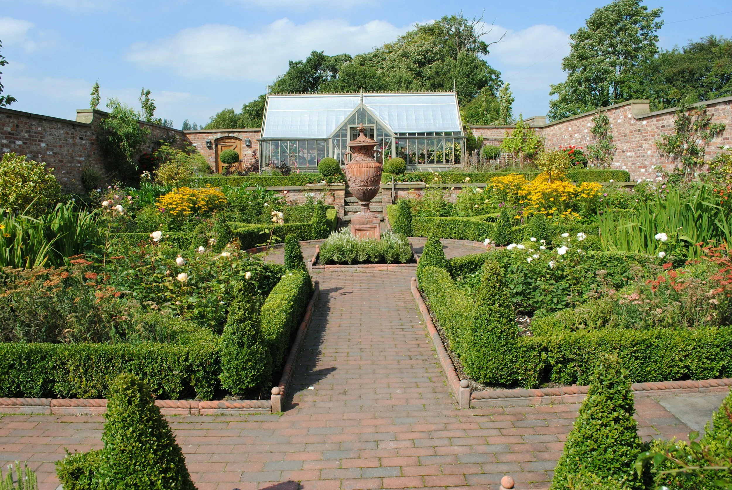 A garden with a stone pathway, filled with colorful flowers and green foliage, and wooden plant supports.