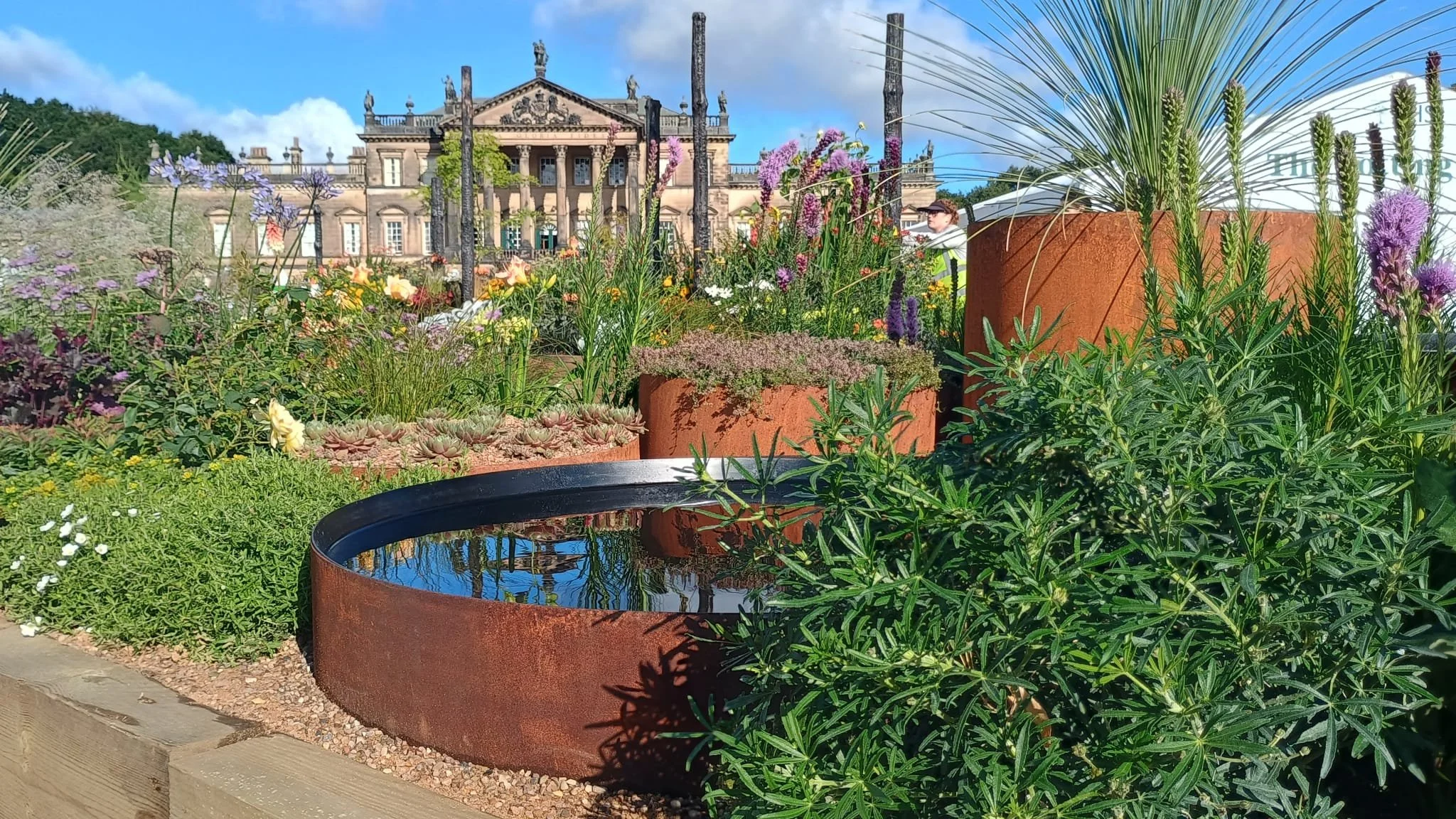Colorful garden with plants and flowers in large rust-colored containers in front of historic building with classical architecture