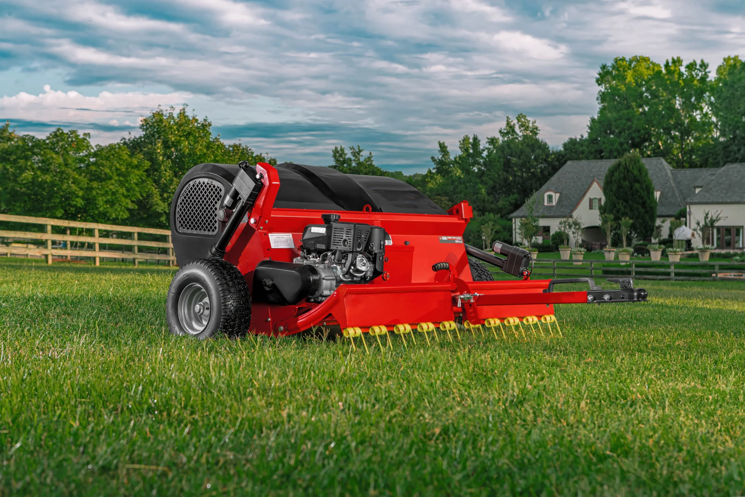 Red commercial mower on a grassy field with a house and trees in the background under a cloudy sky.