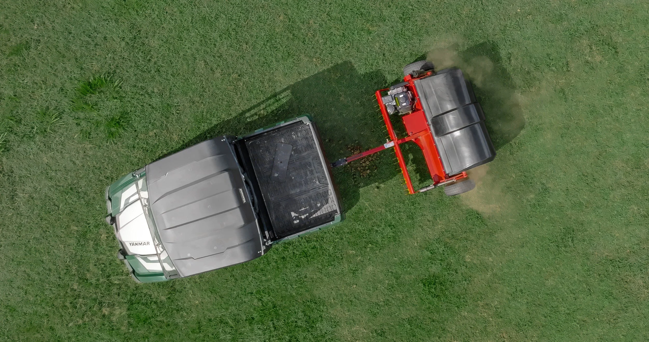 Top-down drone photograph view of a green UTV attached to a red and black Tow and Collect pasture cleaner on a grassy field on an equestrian farm in Landrum, SC near Tryon Equestrian Center.