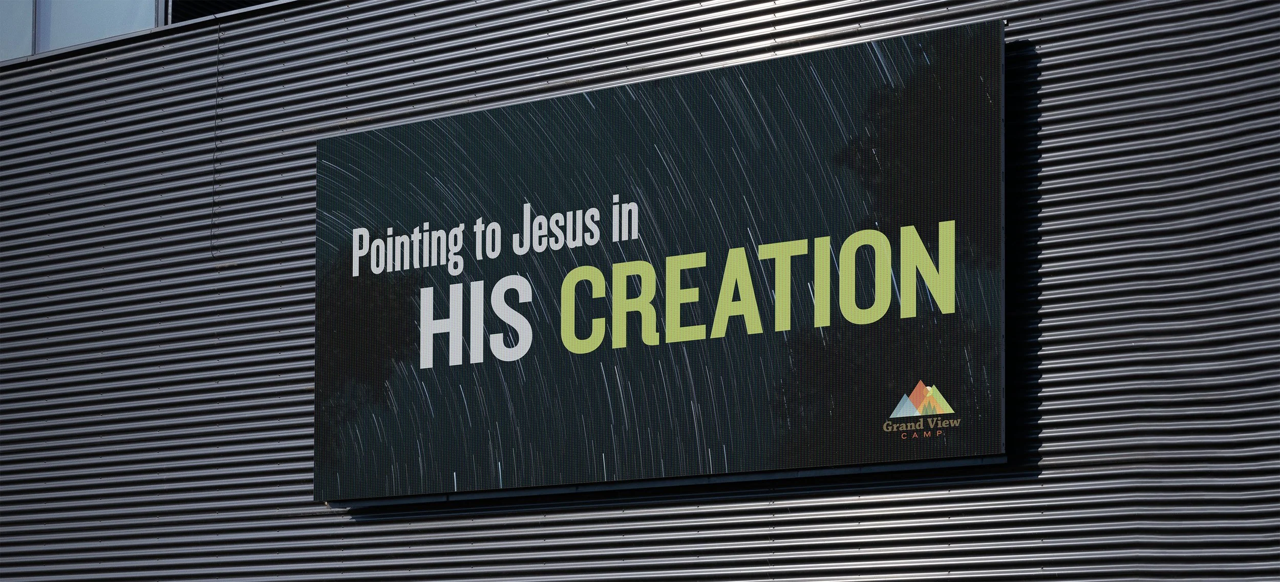 A sign on a building that says, 'Pointing to Jesus in HIS CREATION' with a logo for Grand View Camp in the bottom right corner.