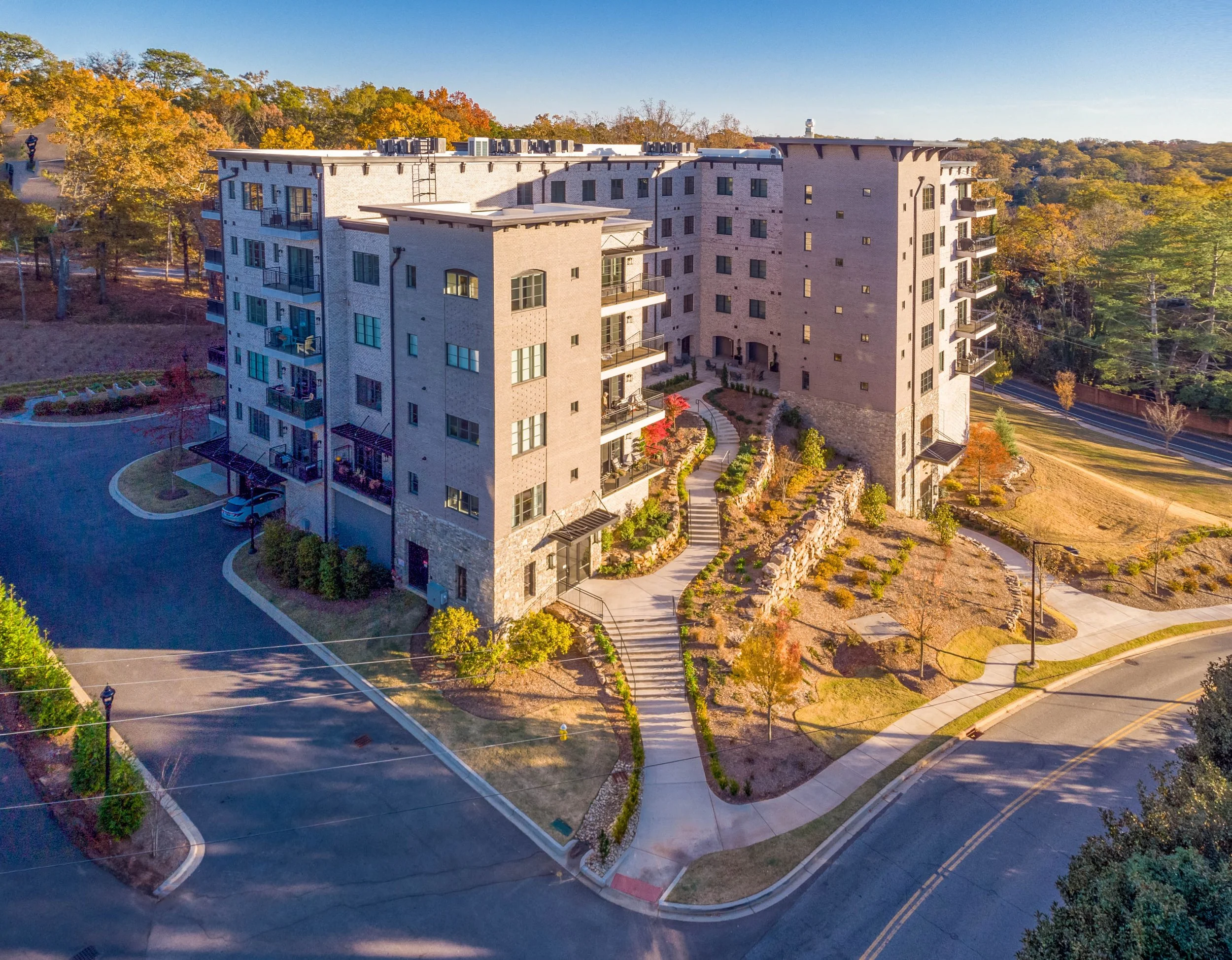 An aerial view of a luxury multi-story residential condominium complex surrounded by landscaped grounds, trees, and quiet streets in downtown Greenville, SC.