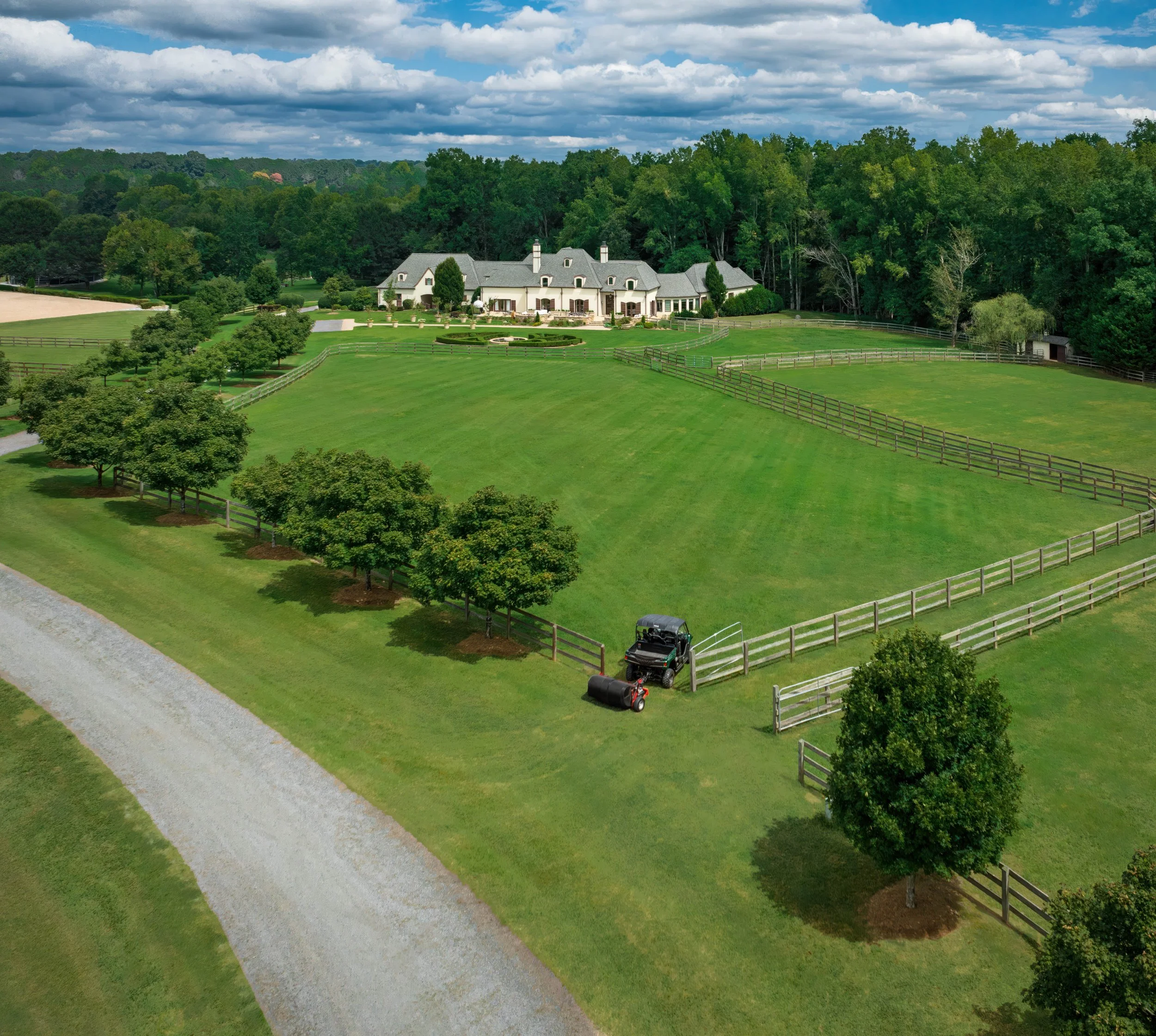 A large estate with a mansion on an equestrian farm, extensive green lawns, trees, and a fenced yard, overcast sky in Landrum, SC, near Tryon Equestrian Center.