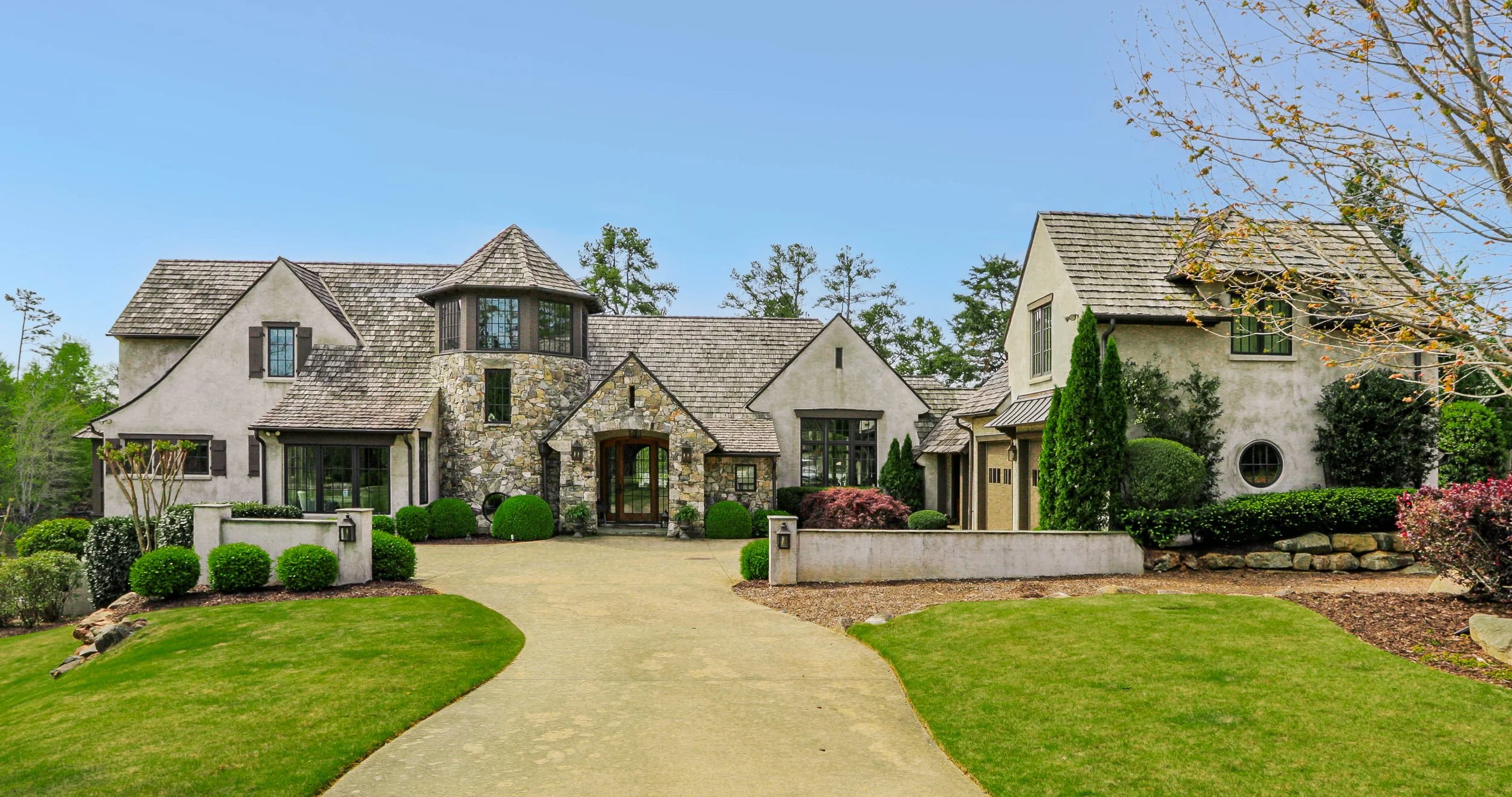 An HDR photograph of a large, professionally painted beige house with a stone entrance, multiple gabled roofs, and a lawn and garden that appears to be manicured by a professional lawn service company in The Reserve on Lake Keowee, SC.
