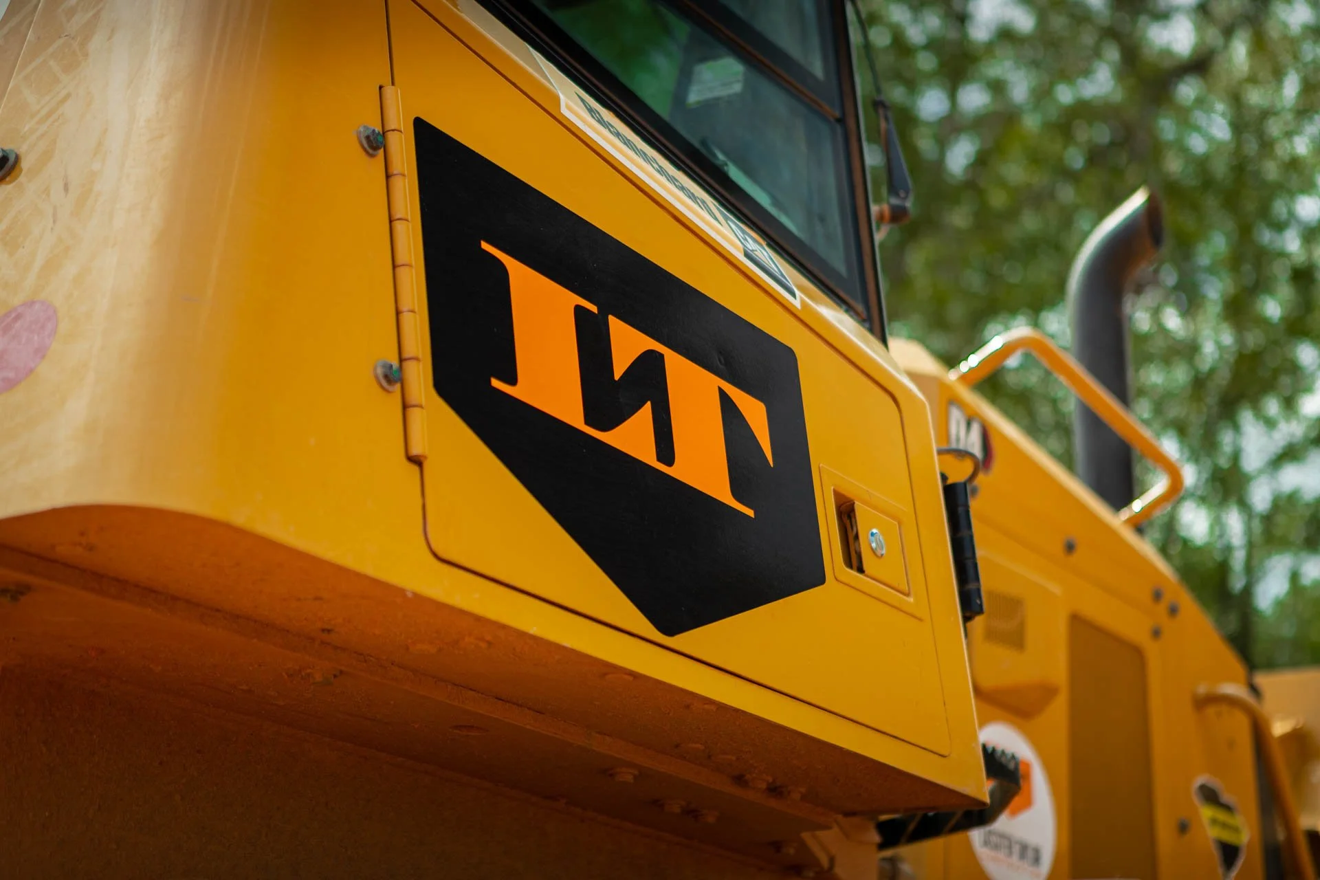 Close-up of a John Deere construction vehicle with a yellow body and black logo, outdoors with trees in the background.
