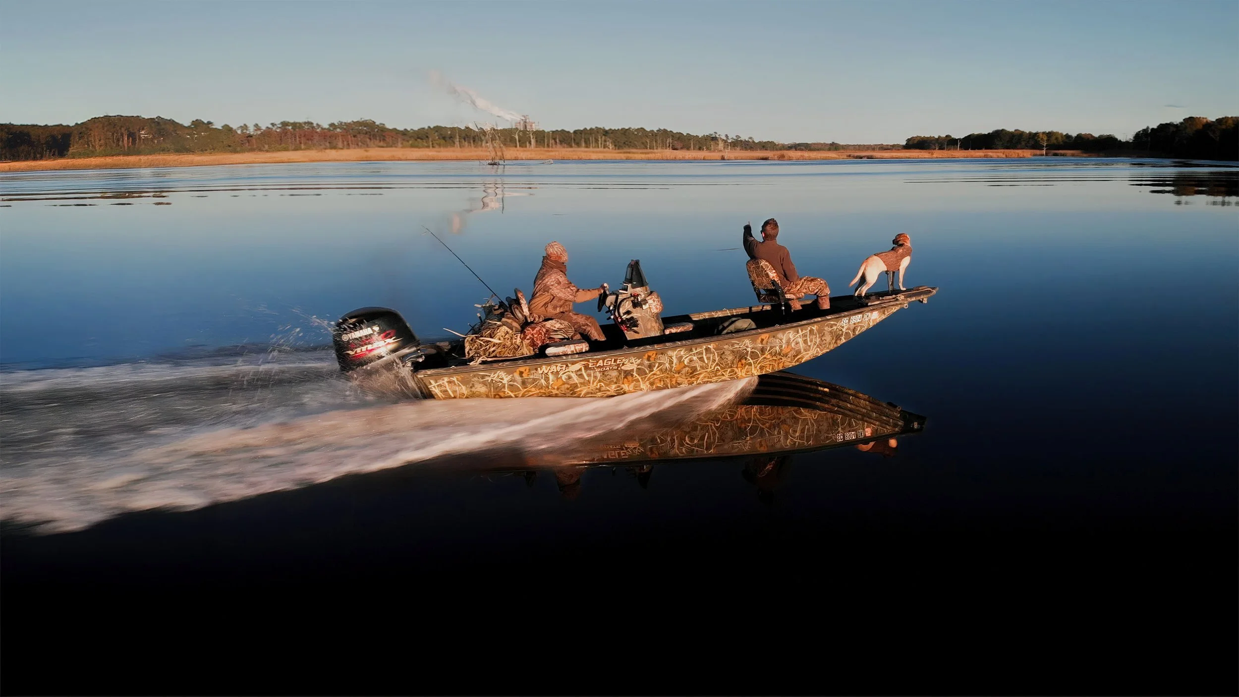 A drone photograph of a camouflaged boat with two hunters and a yellow lab going duck hunting on board moving across Winyah Bay, SC during sunset.