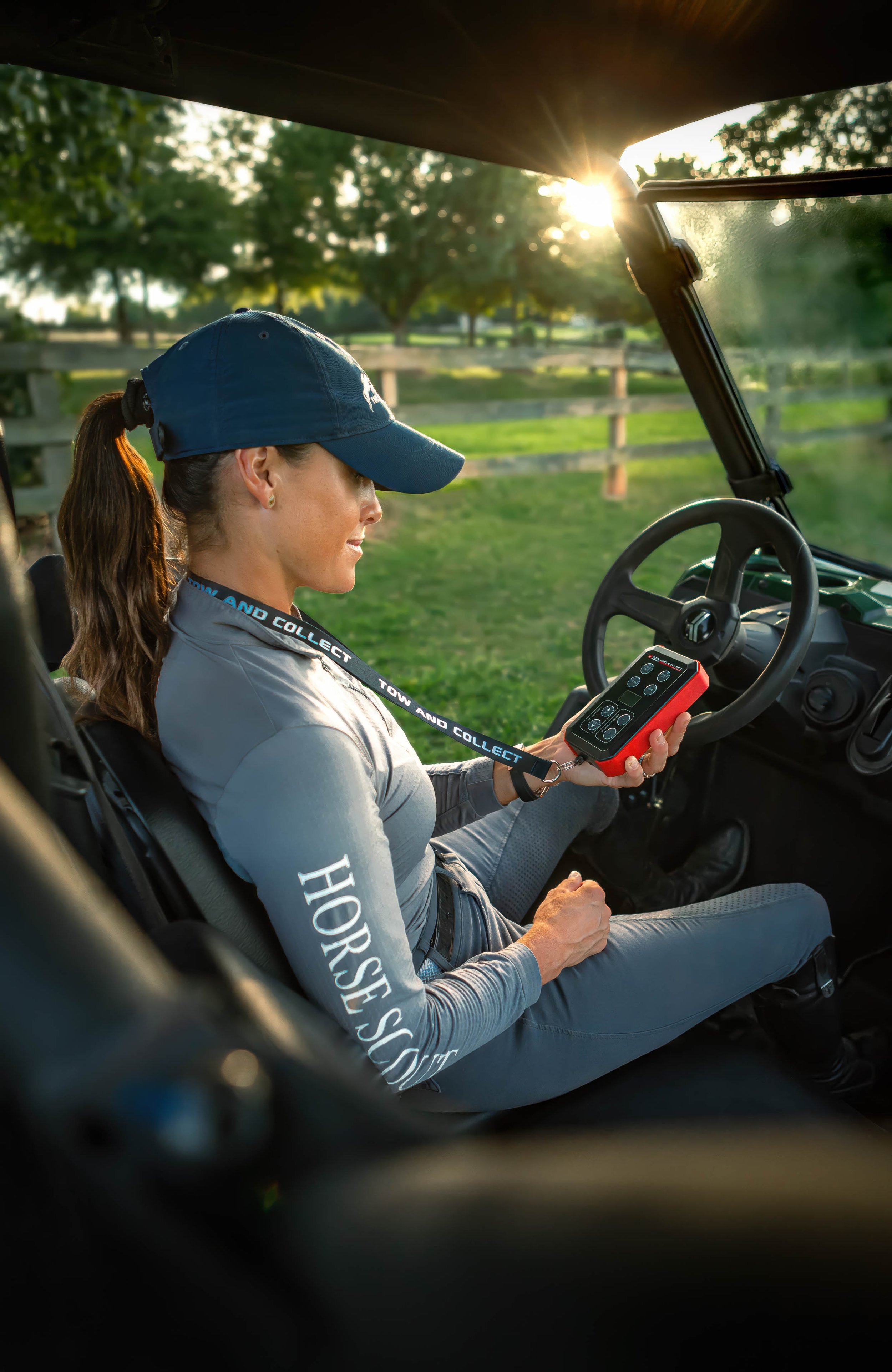 A woman sitting in a golf cart looking at a remote control, with sunlight shining through trees in the background.