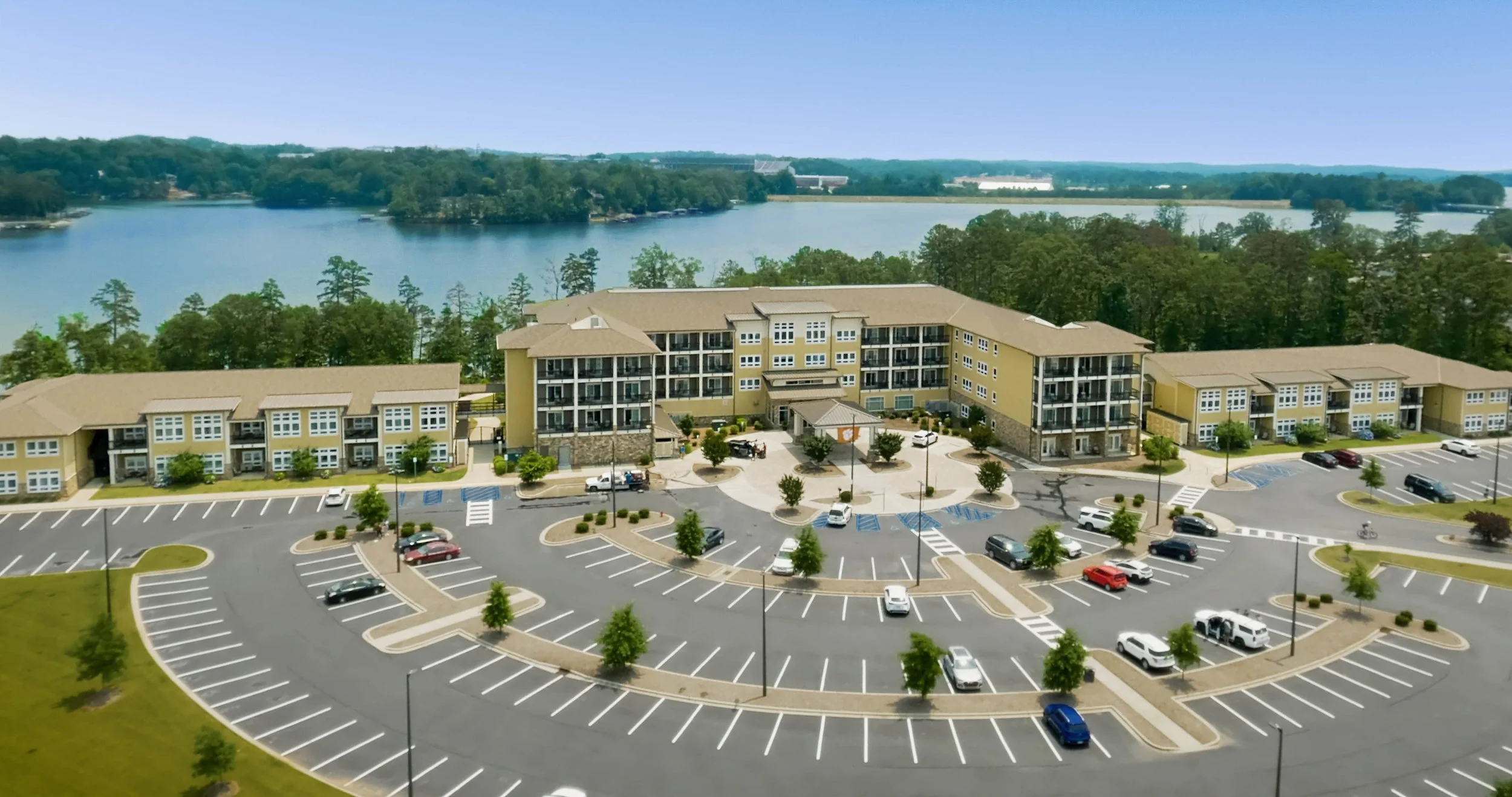 Aerial view of a large apartment complex with a parking lot in front, surrounded by trees and Lake Hartwell, Clemson, SC in the background.