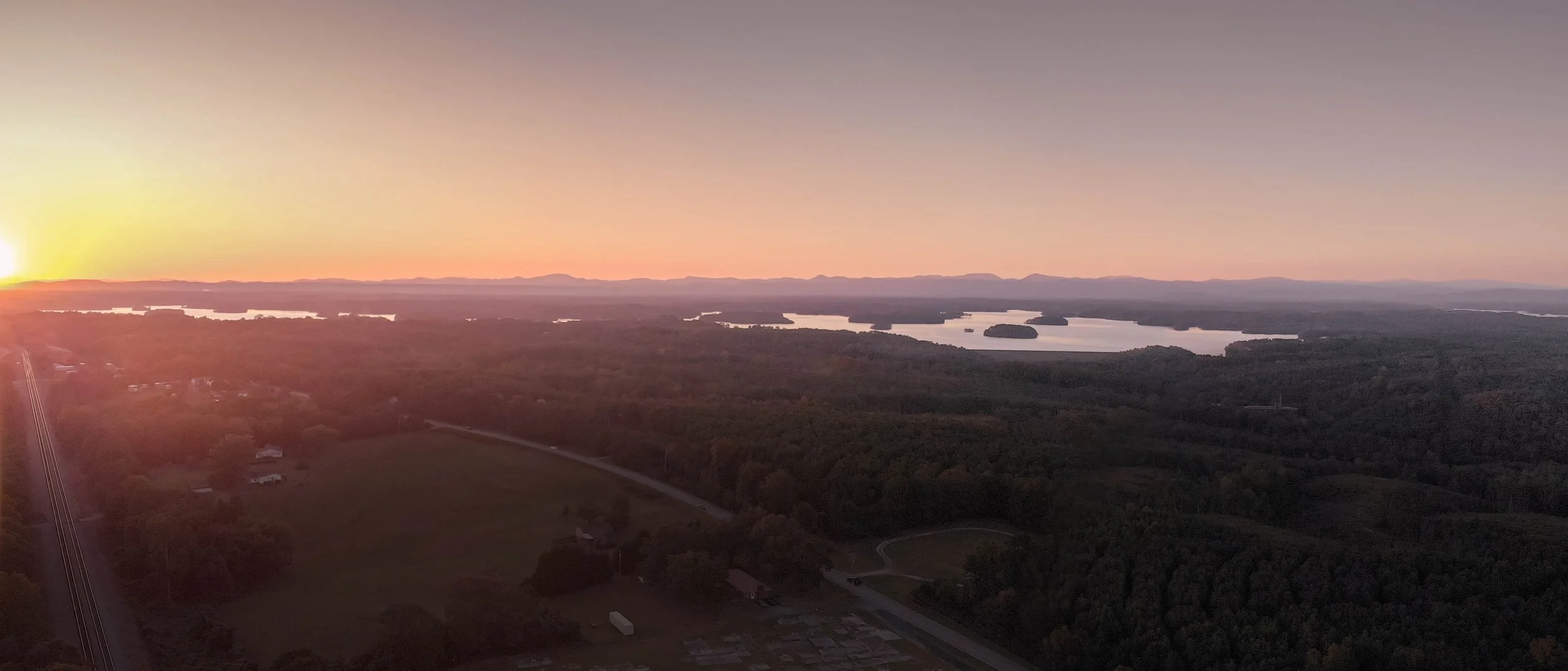 A panoramic drone photograph view of a Lake Keowee, SC at sunset showing lakes, forests, and open fields in Upstate, SC.