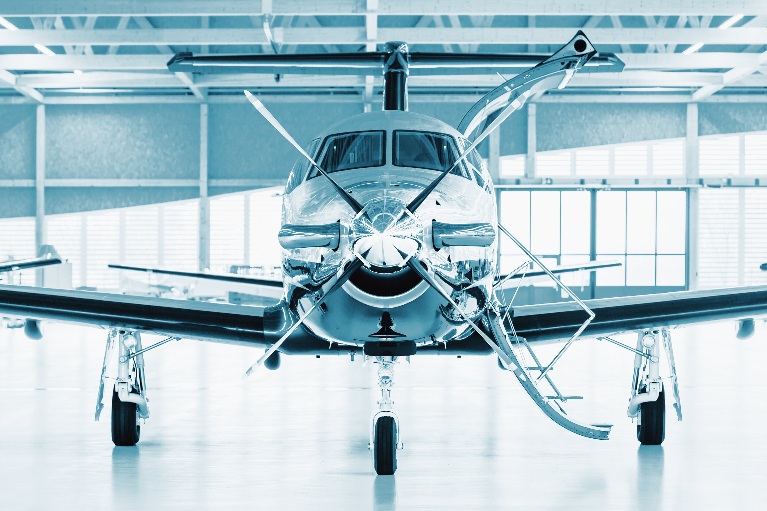 Front view of a sleek, modern helicopter inside a spacious hangar with large windows and overhead beams.
