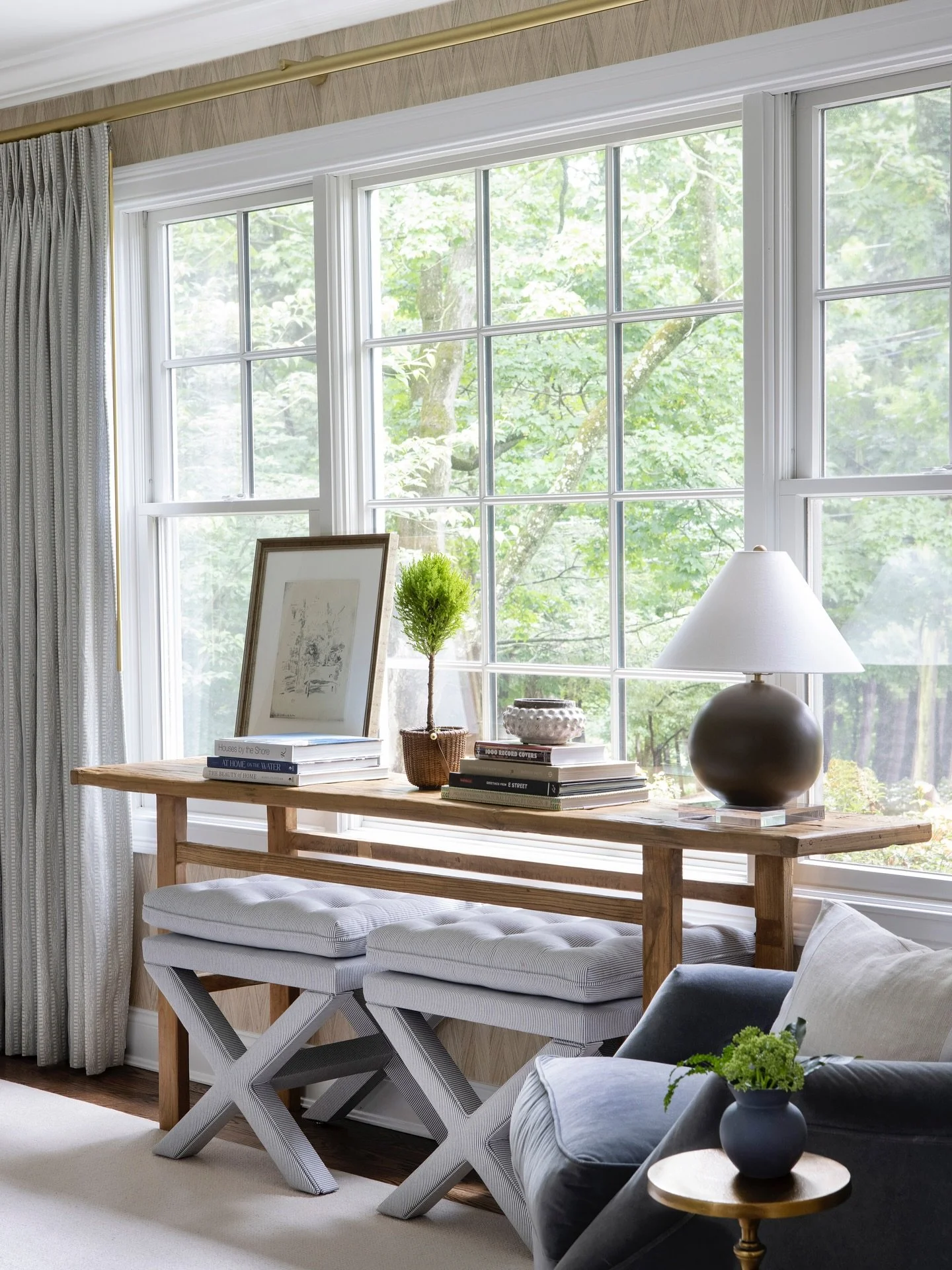 We believe that every inch of your home should reflect both function and feeling. This sunlit nook balances texture, tone, and tailored details &mdash; from the natural wood console and soft upholstered stools to the layered lighting and collected ac
